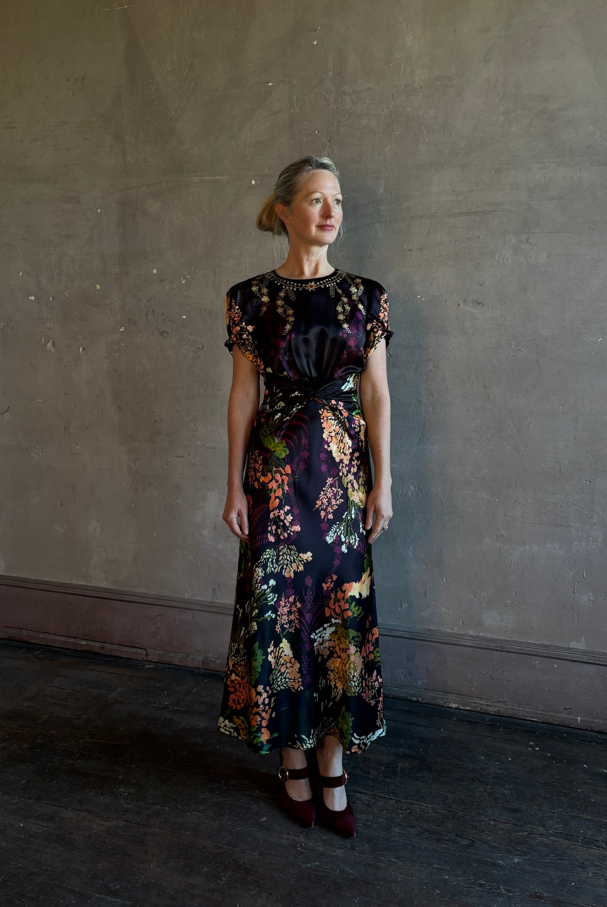 Mature woman wearing Saloni's Gwen C Dress in Equinox Plmt silk blend fit-and-flare silhouette cummerbund waist. Botanical, structured occasion elegance.