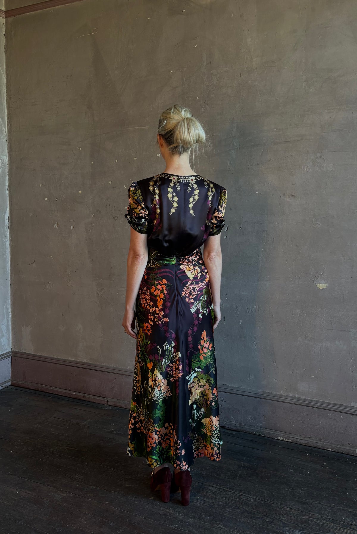 Mature woman wearing Saloni's Gwen C Dress in Equinox Plmt silk blend fit-and-flare silhouette cummerbund waist. Botanical, structured occasion elegance.