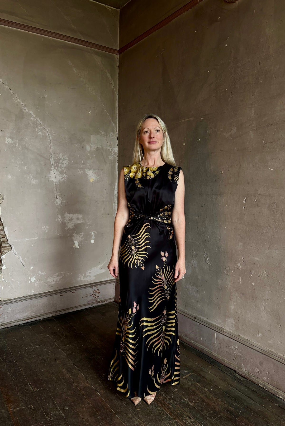 Mature woman wearing Saloni Gwen Dress in Golden Palm semi-open back gathered waist black with yellow and pink print evening gown