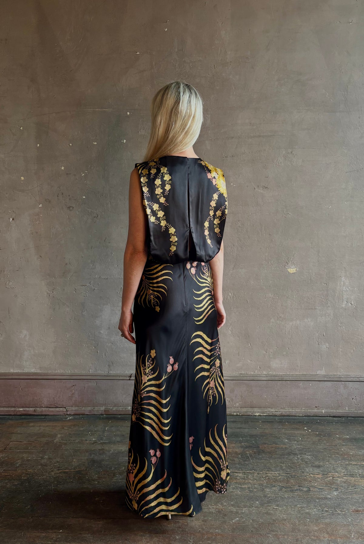 Mature woman wearing Saloni Gwen Dress in Golden Palm semi-open back gathered waist black with yellow and pink print evening gown