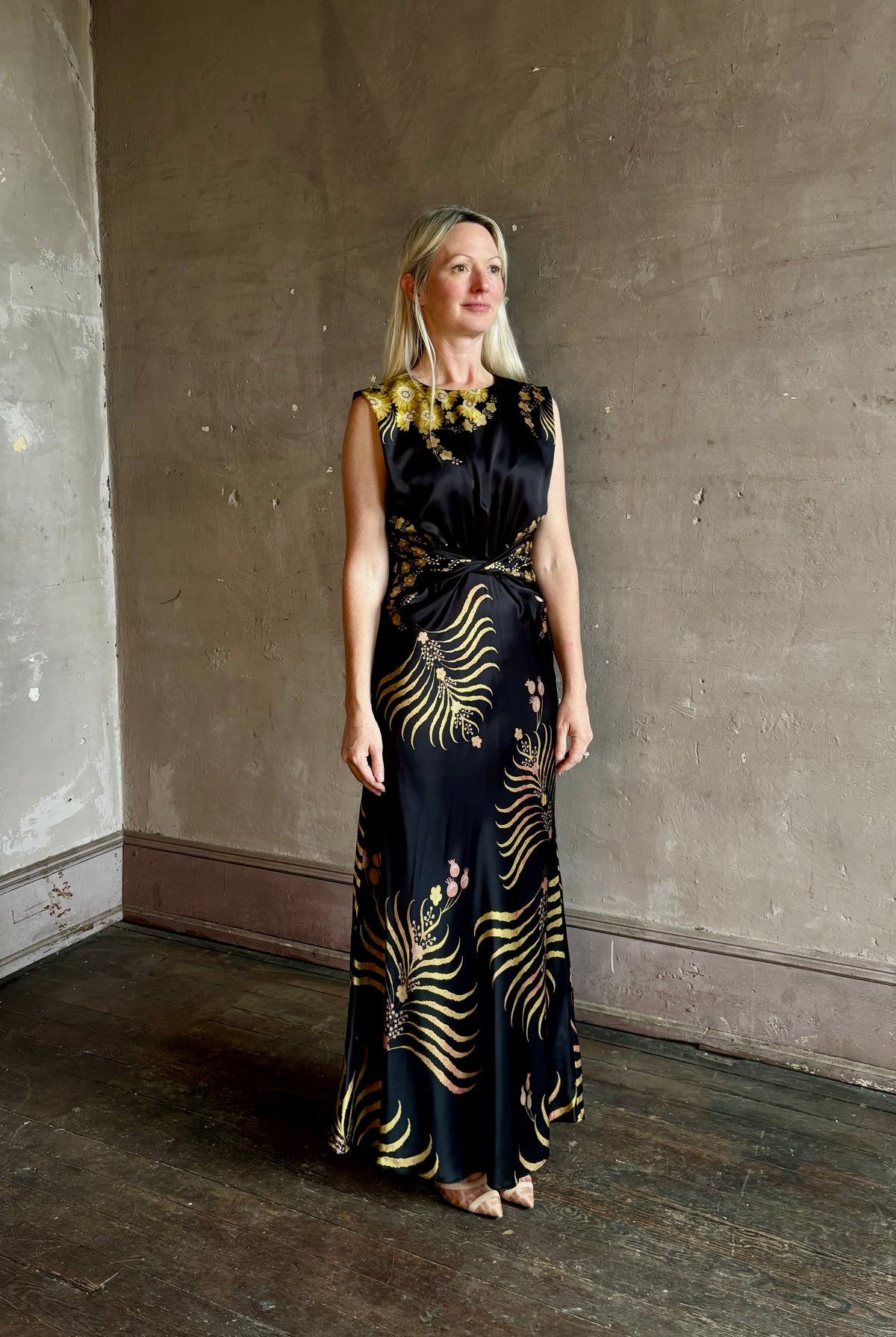 Mature woman wearing Saloni Gwen Dress in Golden Palm semi-open back gathered waist black with yellow and pink print evening gown
