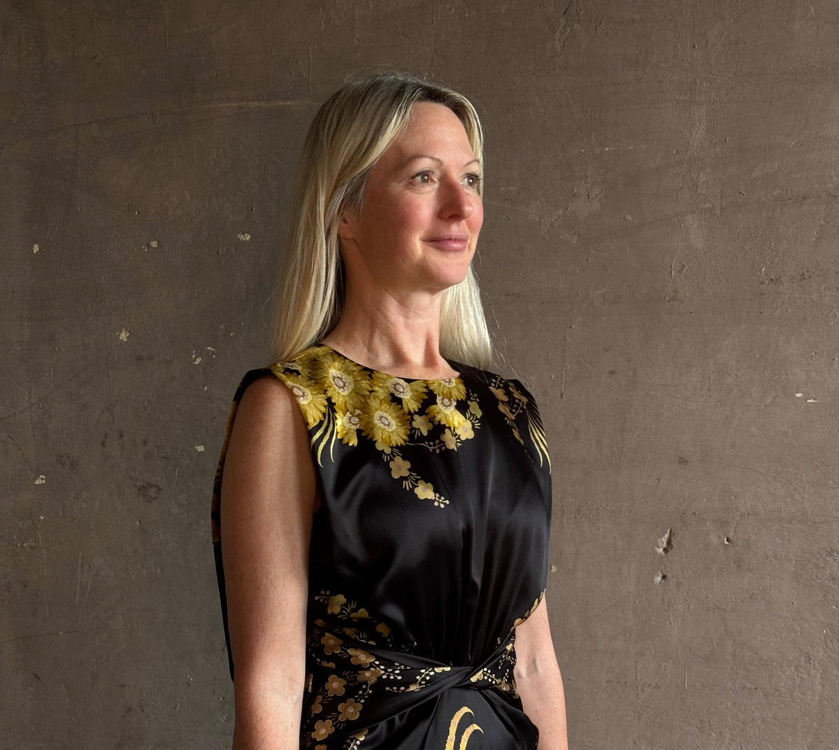 Mature woman wearing Saloni Gwen Dress in Golden Palm semi-open back gathered waist black with yellow and pink print evening gown