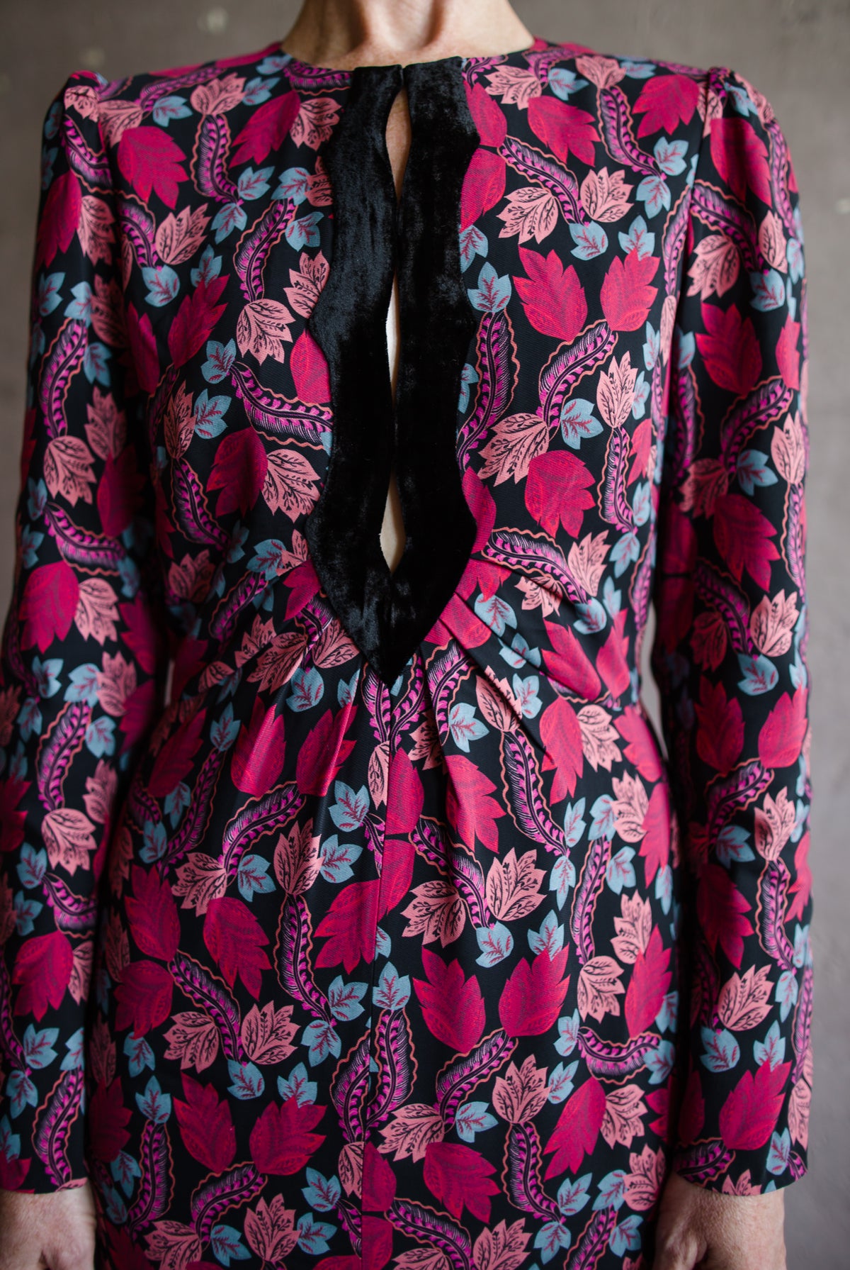 Mature woman wearing the Jinx-C Maxi dress by Saloni crew neckline, long sleeves, and velvet trim cutouts down the front Follium Rouge and black print