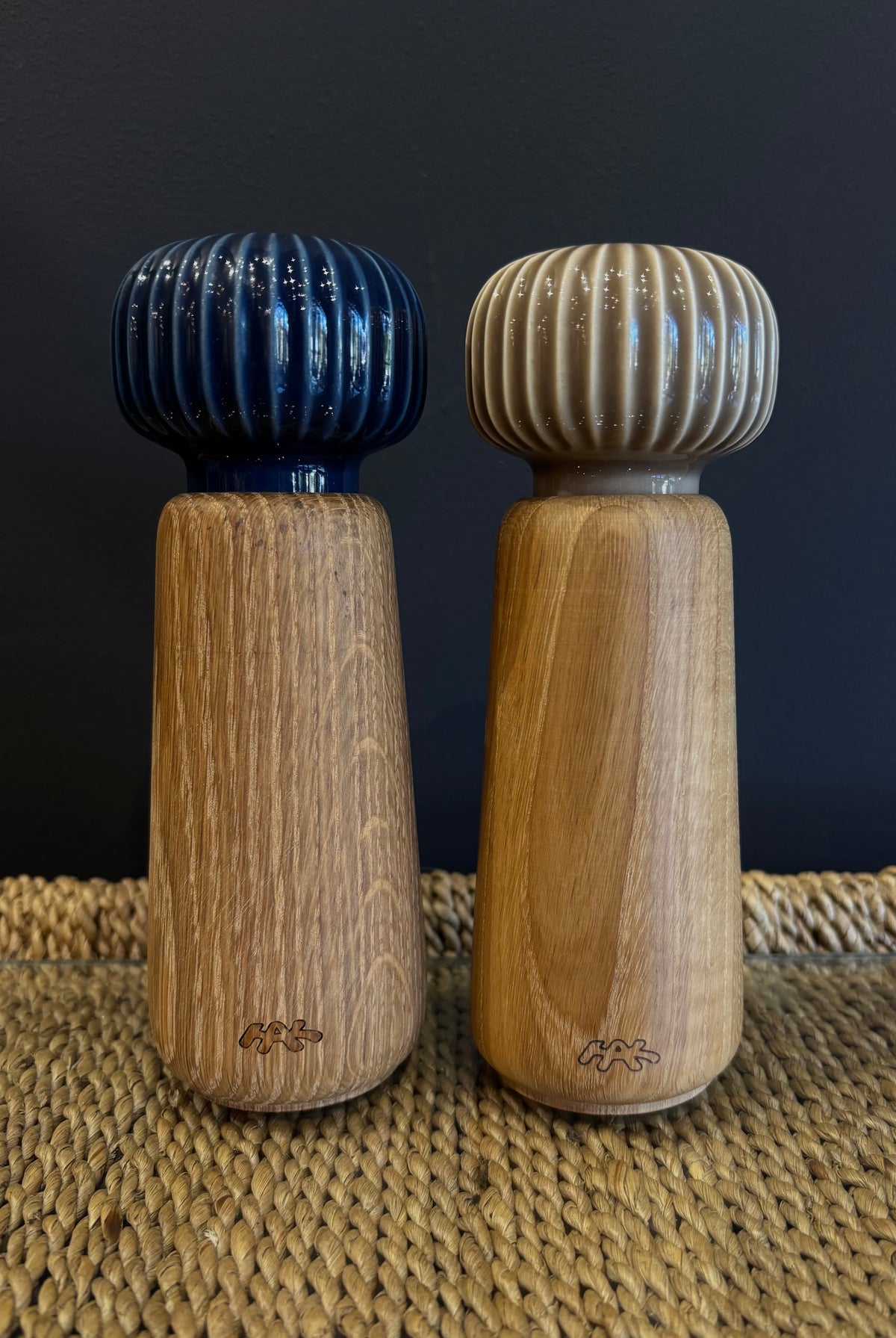 A wooden spice grinder set with a neutral taupe beige and navy blue ribbed ceramic top and a natural finish oak wood body