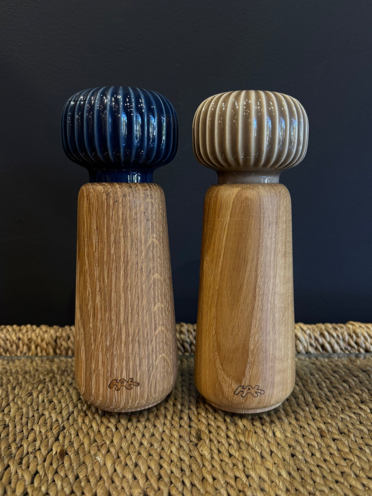 A wooden spice grinder set with a neutral taupe beige and navy blue ribbed ceramic top and a natural finish oak wood body