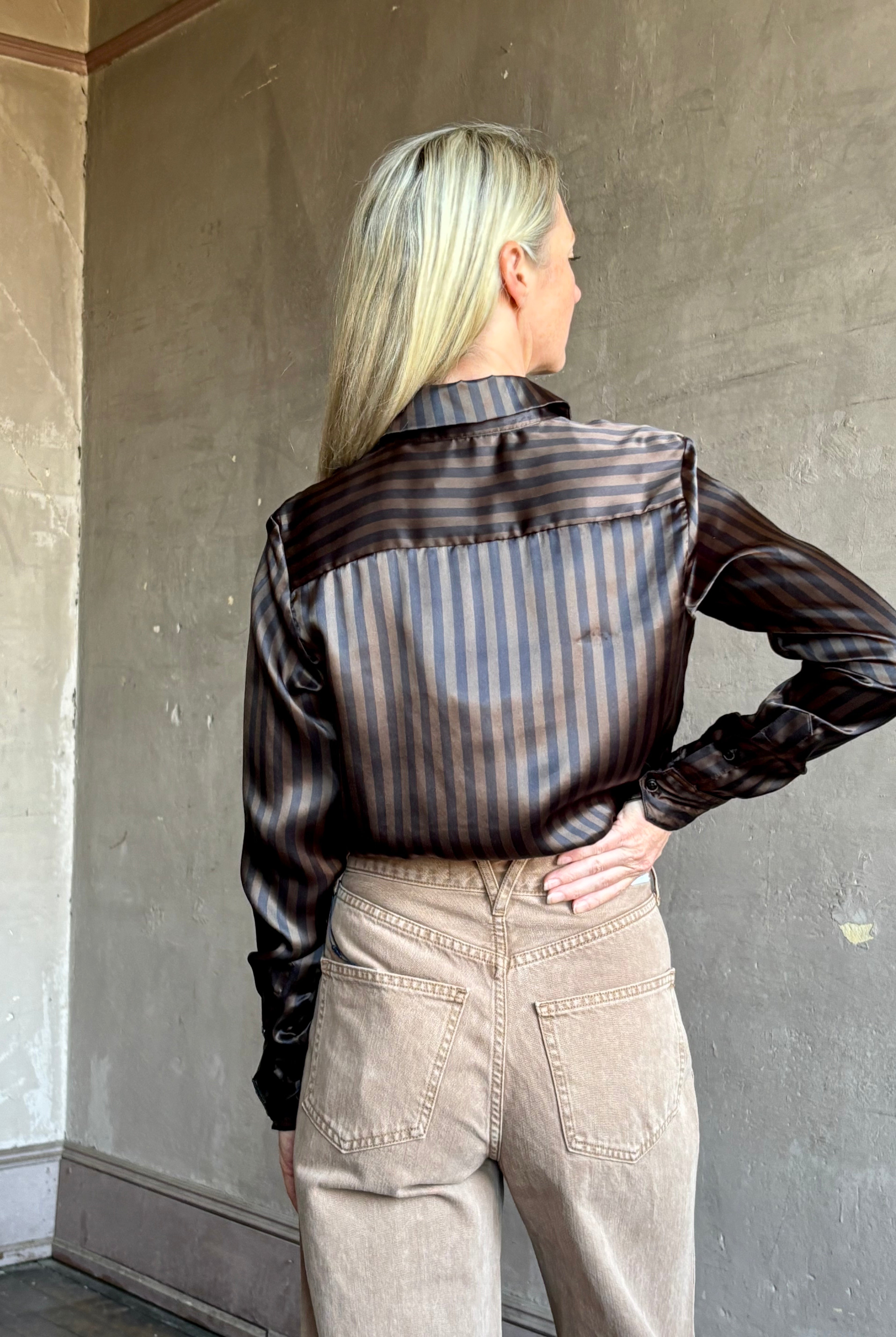 Image of woman wearing luxury brand SPRWMN Fonda silk button up shirt in a black and brown stripe modern classic.