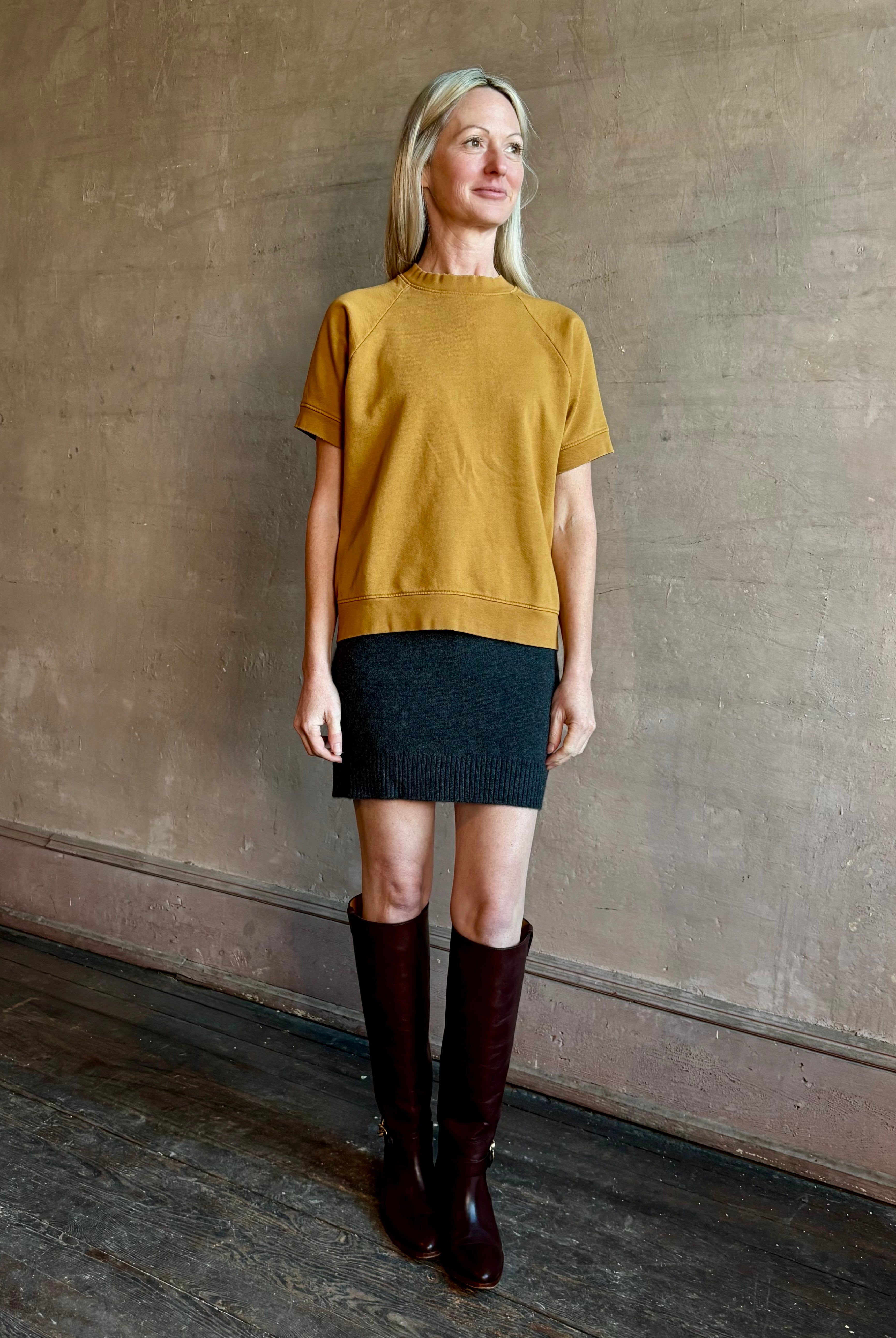 Image of woman wearing SPRWMN Mia cashmere skirt in charcoal grey with a Rachel Comey yellow sweatshirt and tall boots