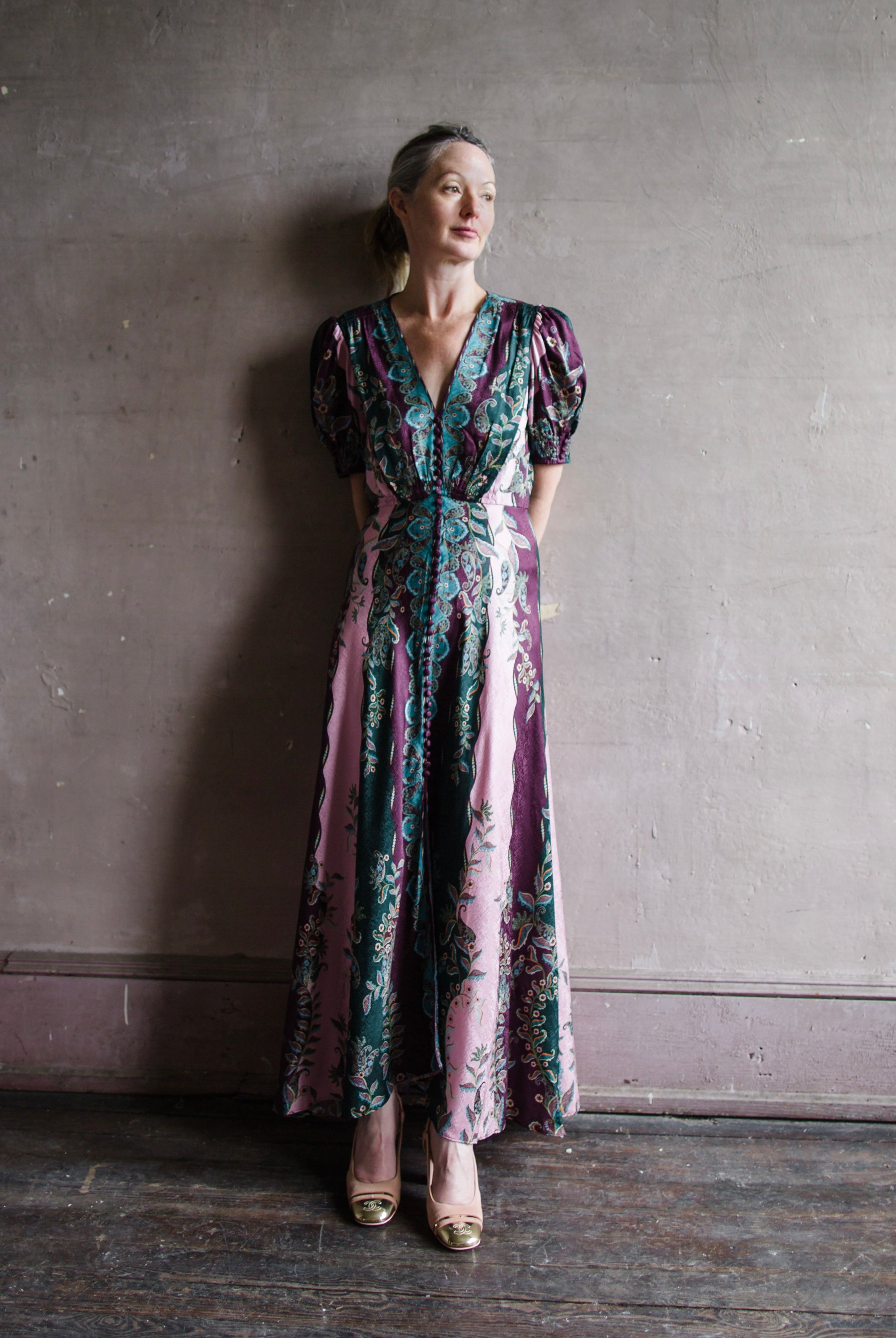 Image featuring a woman wearing the Lea Long silk Dress by Saloni with a v neckline, button front, puff short sleeves and a tailored waist in stripe plum, teal, & pink.