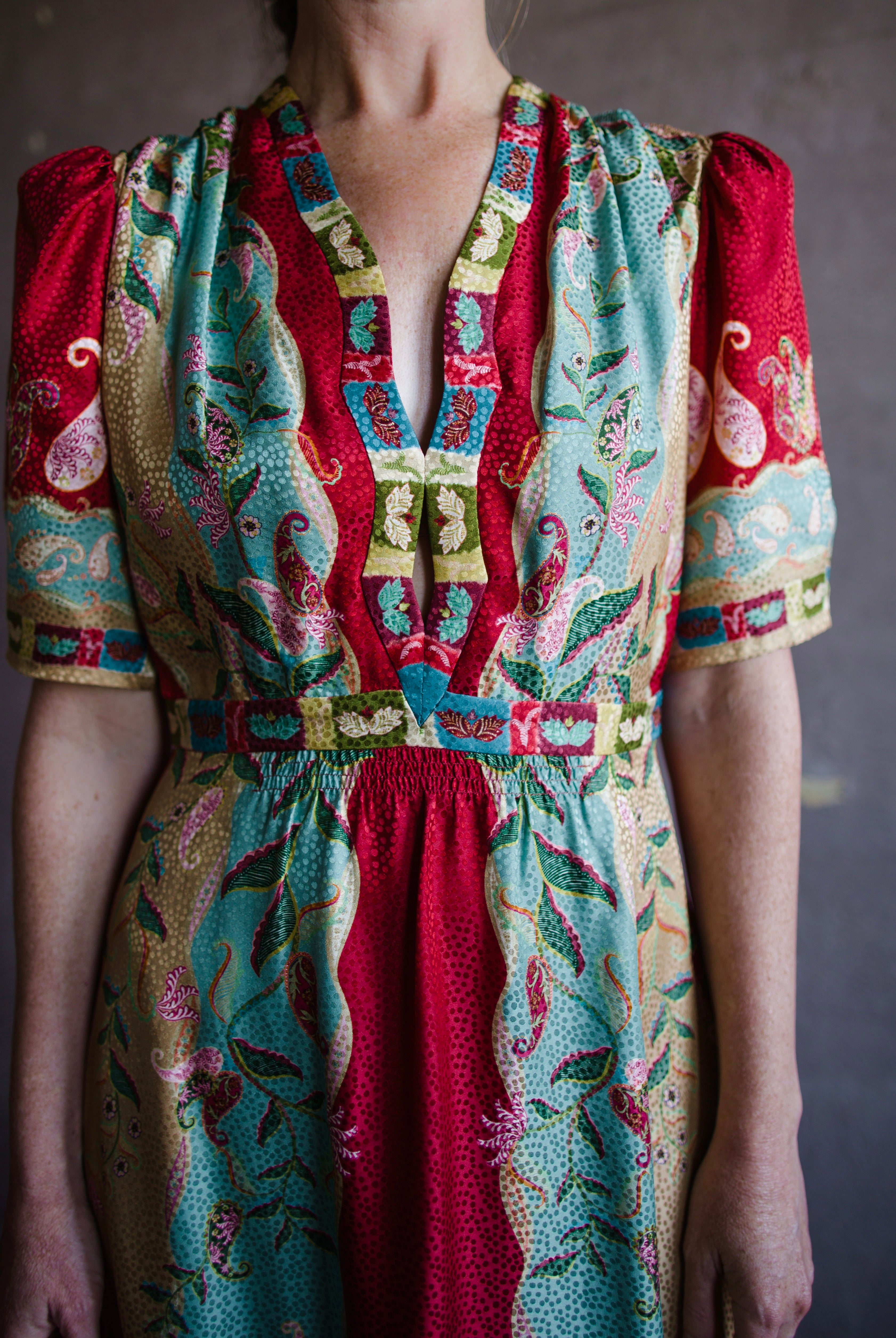 Image featuring a woman wearing the Tabitha silk dress by Saloni with a v neckline, puff short sleeves and a cinched waist in red, yellow, and aqua floral print.