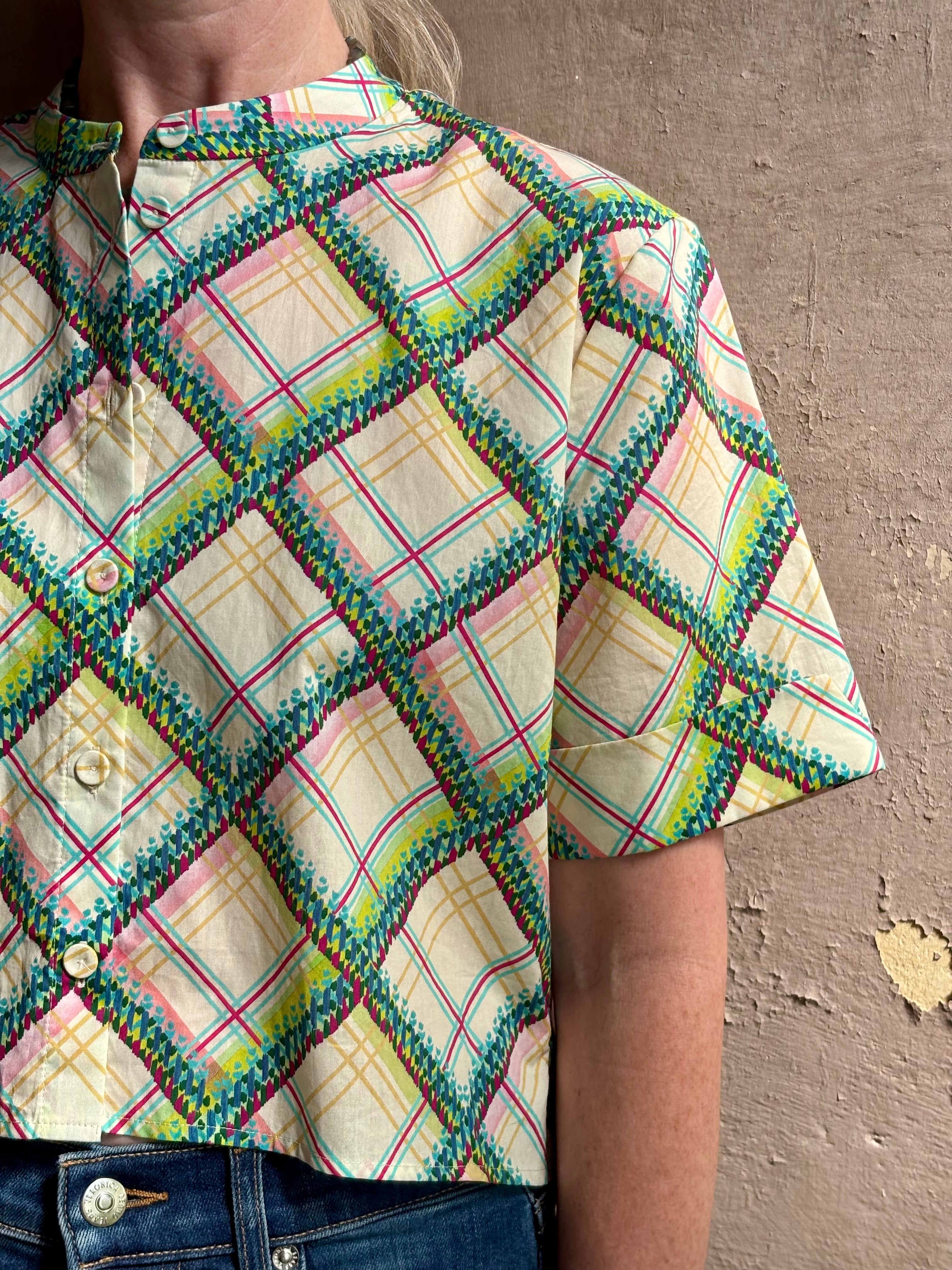 Mature woman wearing the Saloni Jude-B short sleeve plaid button up crop top crafted in cotton with happy diagonal green, yellow, aqua and pink plaid expertly aligned pattern