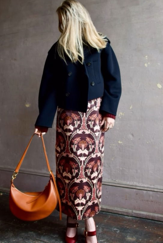 Image of woman wearing Cara Cara Blaze Skirt in Arcada Chocolate cotton-spandex construction with elegant Morris floral print, raffia belt, and straight hem