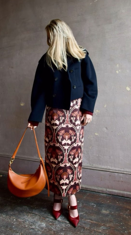 Image of woman wearing Cara Cara Blaze Skirt in Arcada Chocolate cotton-spandex construction with elegant Morris floral print, raffia belt, and straight hem