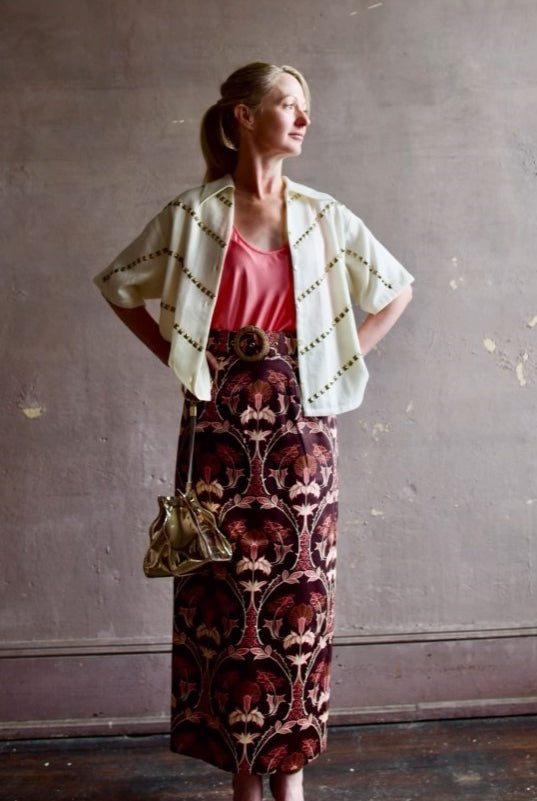 Image of woman wearing Cara Cara Blaze Skirt in Arcada Chocolate cotton-spandex construction with elegant Morris floral print, raffia belt, and straight hem
