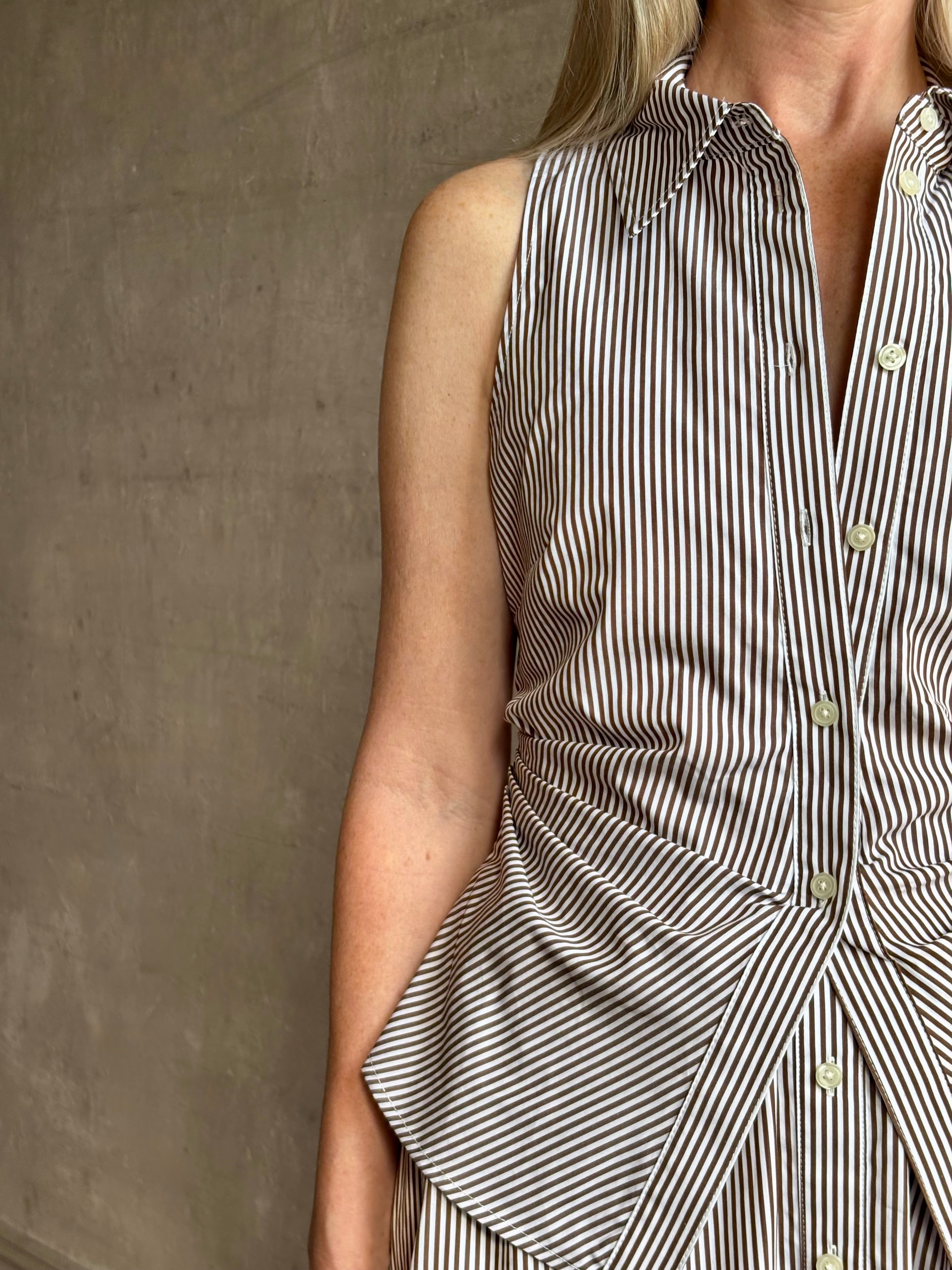 Mature woman wearing the Hannah maxi shirt dress from designer Tanya Taylor rendered in a brown and white stripe and crafted from 100% cotton poplin with a very classy flattering waistline that doesn't stick to body, sleeveless with a collar for a timeless tailored classic dress