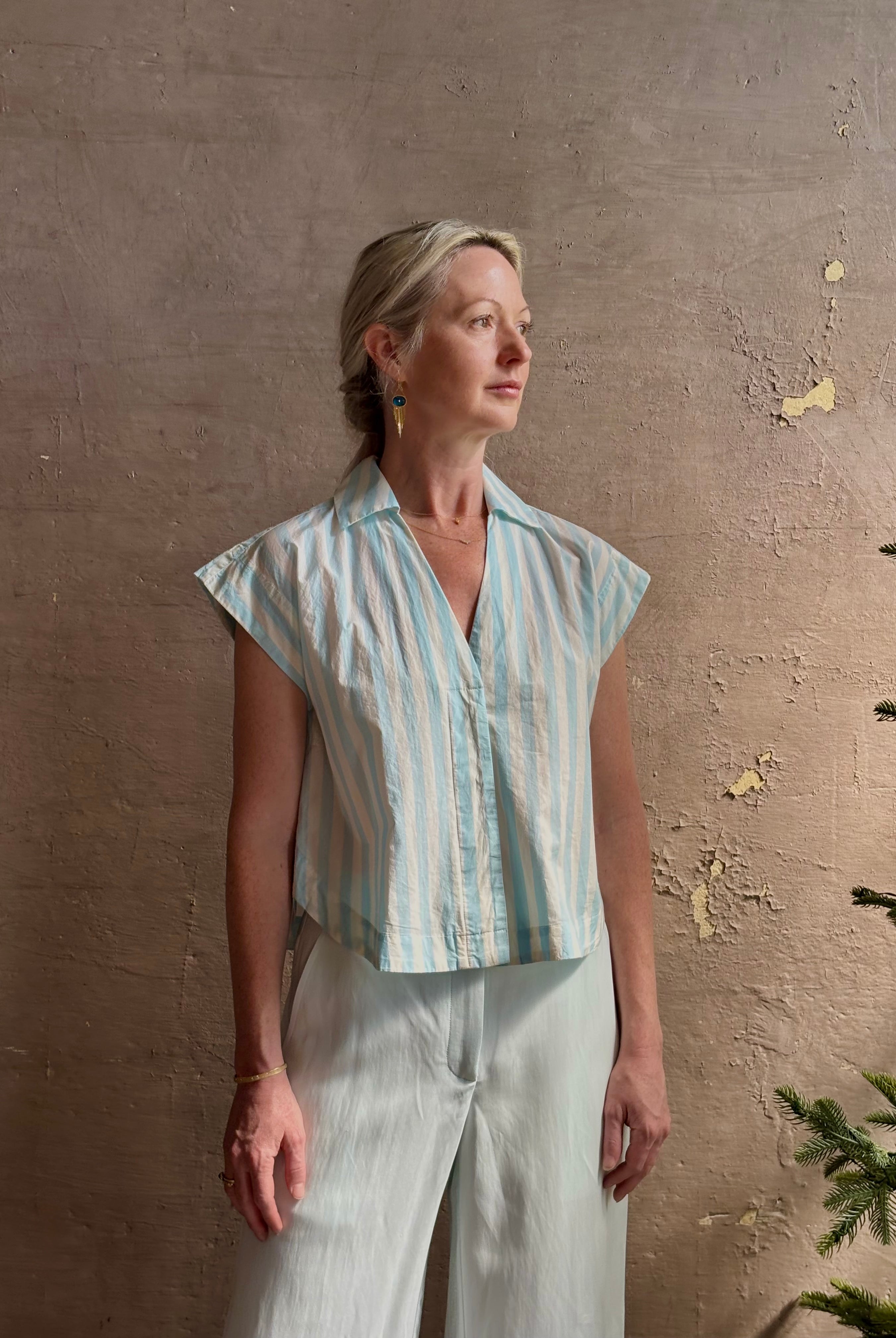 Mature woman wearing Dorada short sleeve Shirt from Trovata rendered in a fresh aqua and cream Stripe and crafted from cotton poplin with v-neck, collar and consealed button front