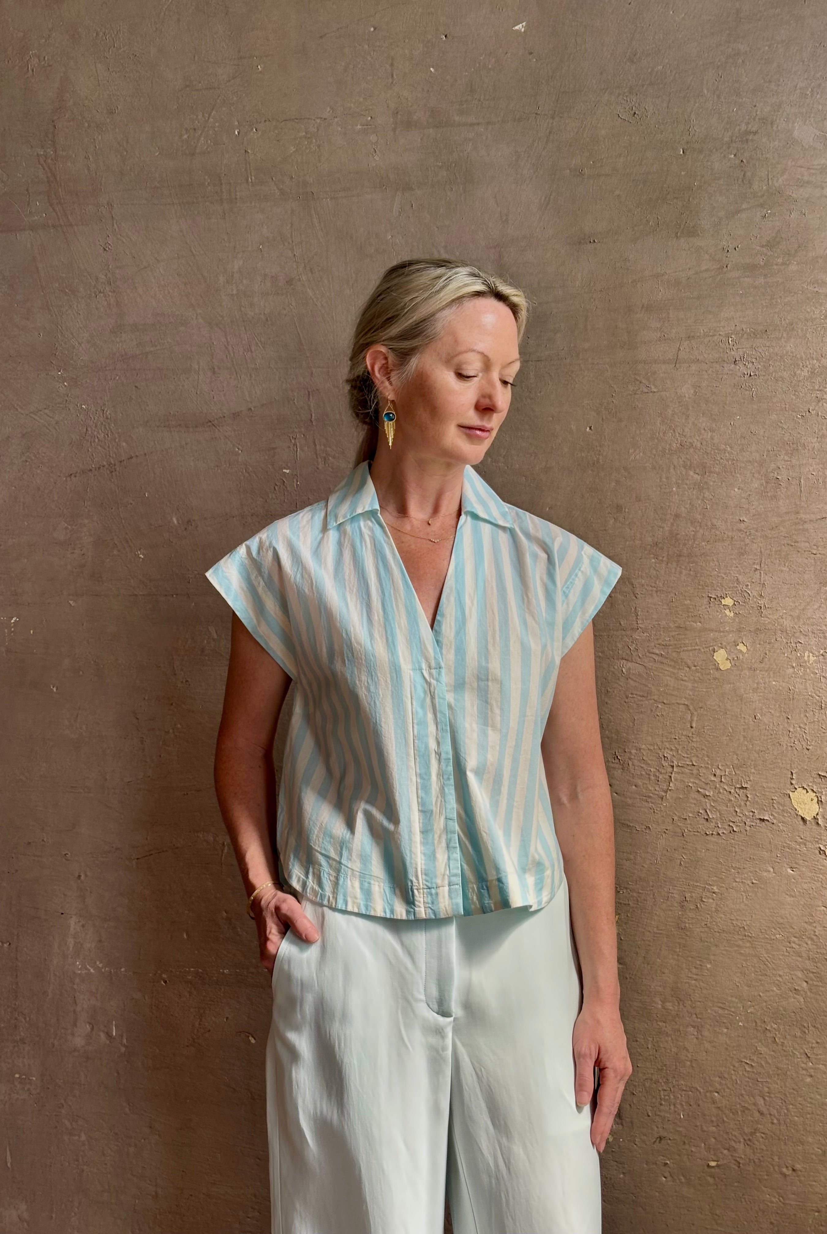 Mature woman wearing Dorada short sleeve Shirt from Trovata rendered in a fresh aqua and cream Stripe and crafted from cotton poplin with v-neck, collar and consealed button front