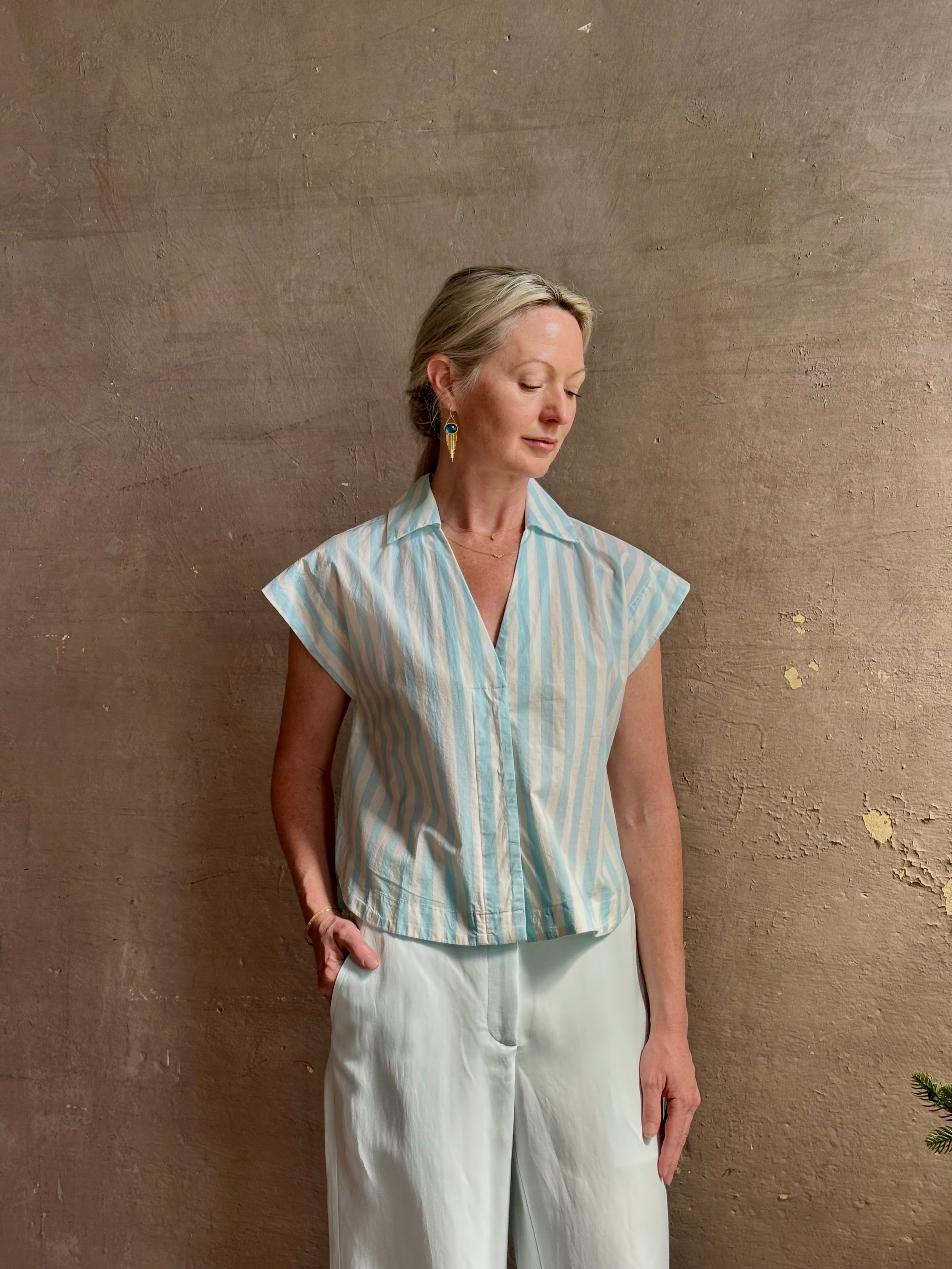 Mature woman wearing Dorada short sleeve Shirt from Trovata rendered in a fresh aqua and cream Stripe and crafted from cotton poplin with v-neck, collar and consealed button front