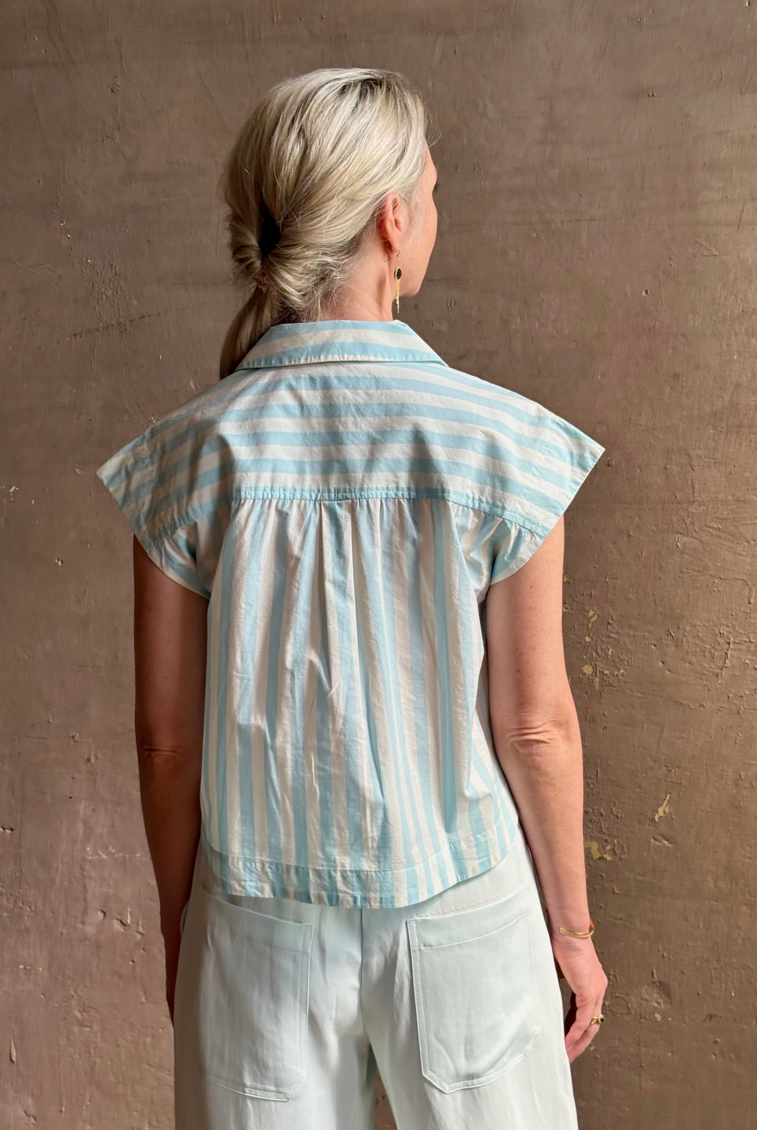 Mature woman wearing Dorada short sleeve Shirt from Trovata rendered in a fresh aqua and cream Stripe and crafted from cotton poplin with v-neck, collar and consealed button front