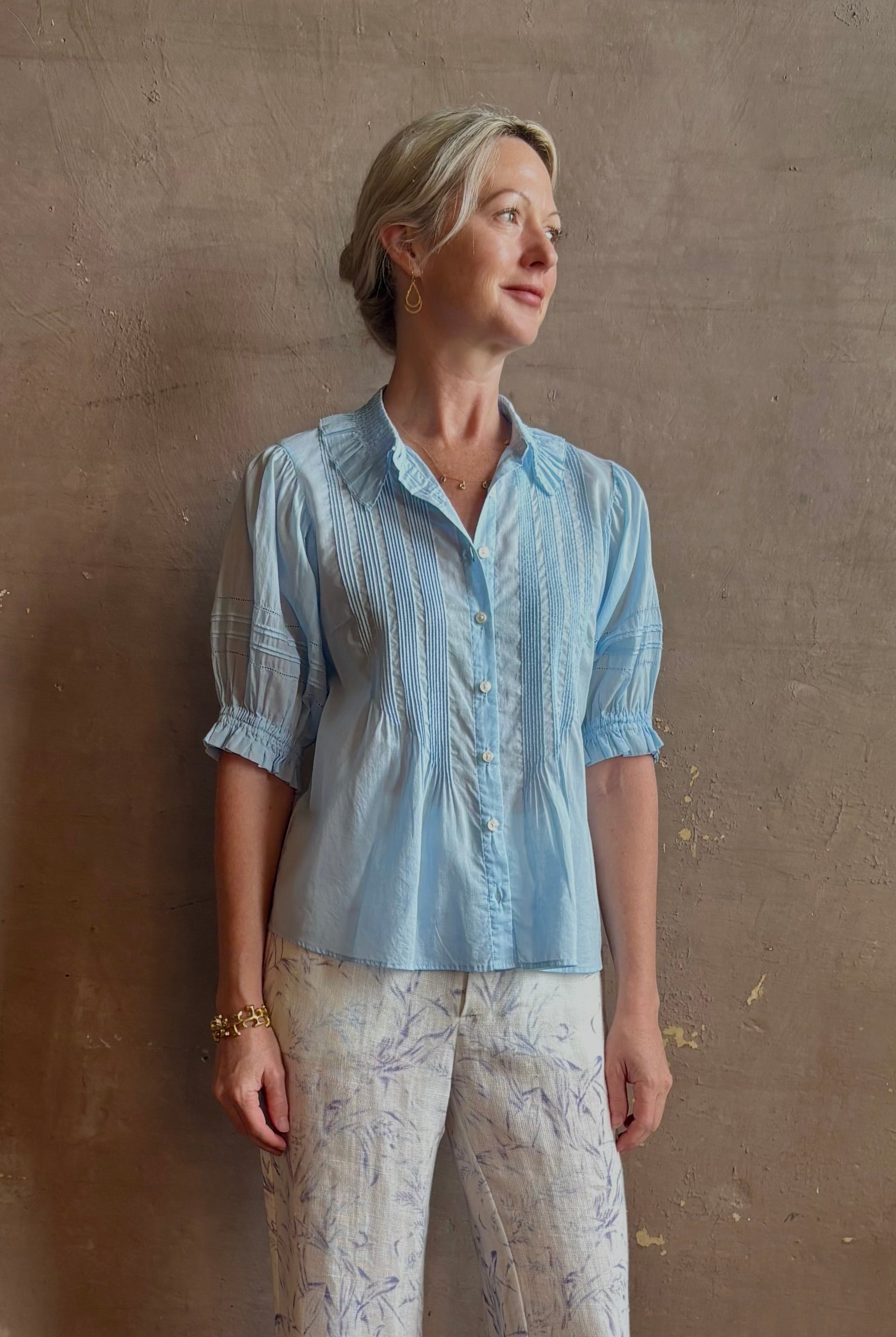 Mature woman wearing Jess Blouse from Trovata rendered in the light blur and crafted from cotton poplin with peter pan collar, half sleeves, intricate pitucking and button front
