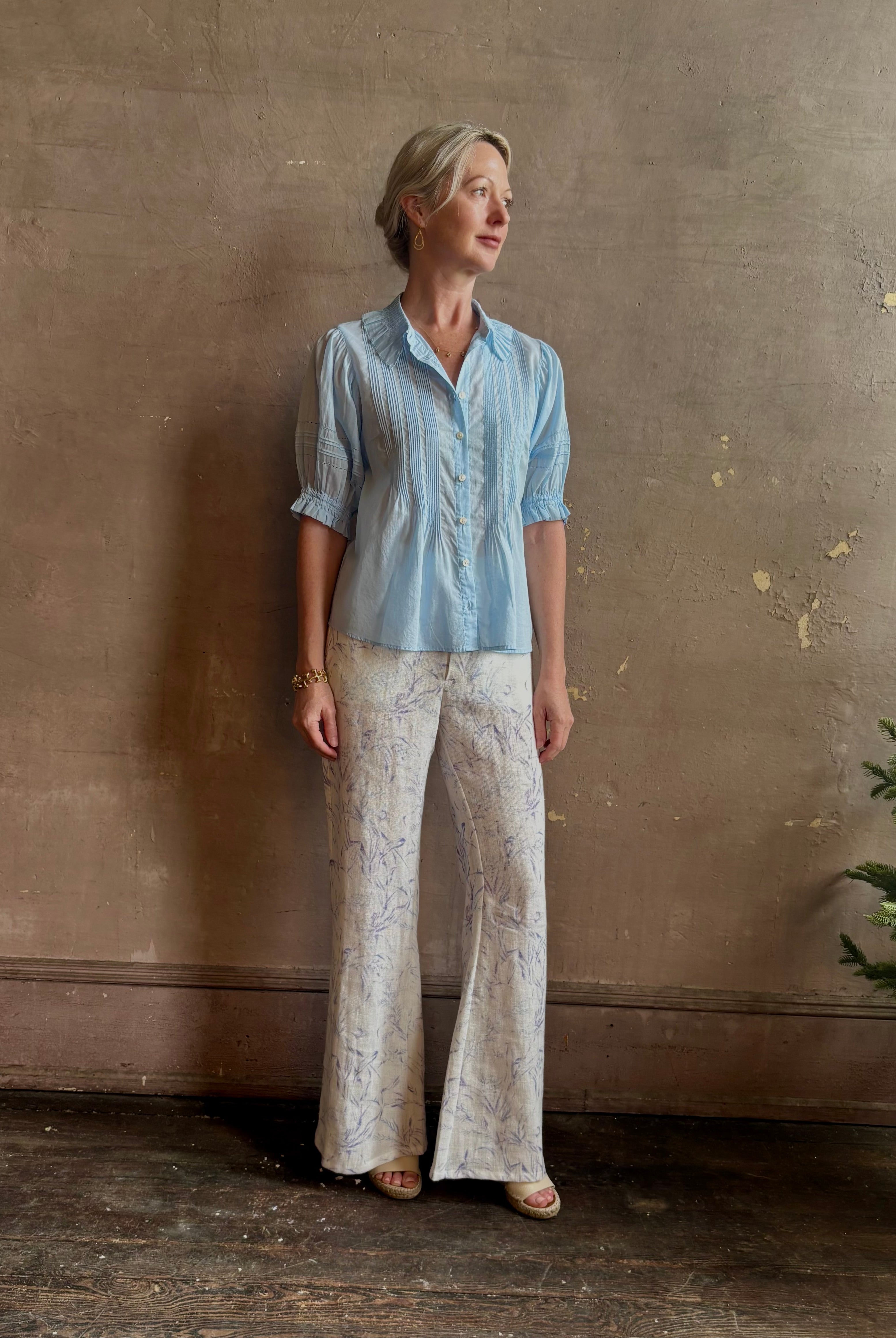 Mature woman wearing Jess Blouse from Trovata rendered in the light blur and crafted from cotton poplin with peter pan collar, half sleeves, intricate pitucking and button front