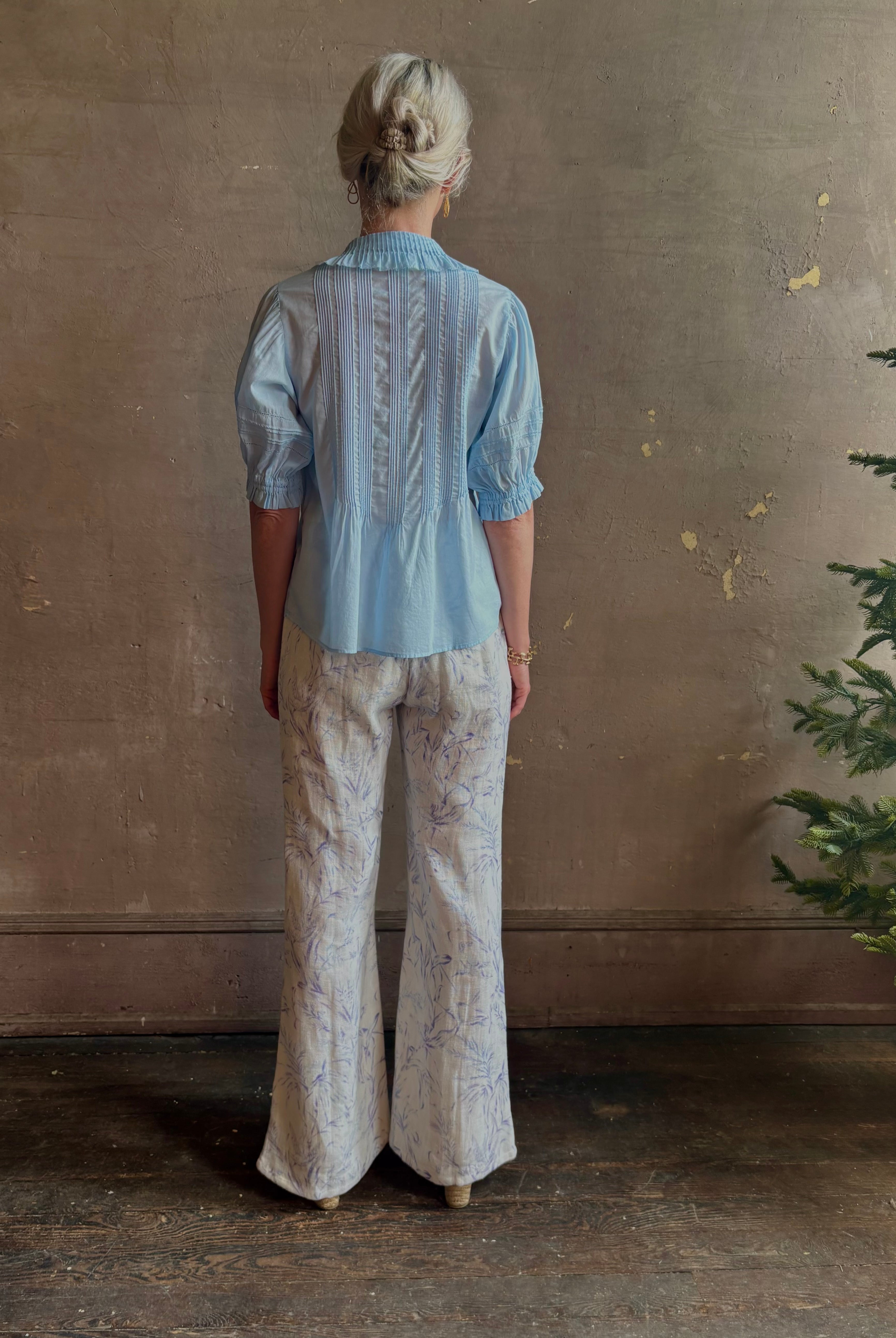 Mature woman wearing Jess Blouse from Trovata rendered in the light blur and crafted from cotton poplin with peter pan collar, half sleeves, intricate pitucking and button front