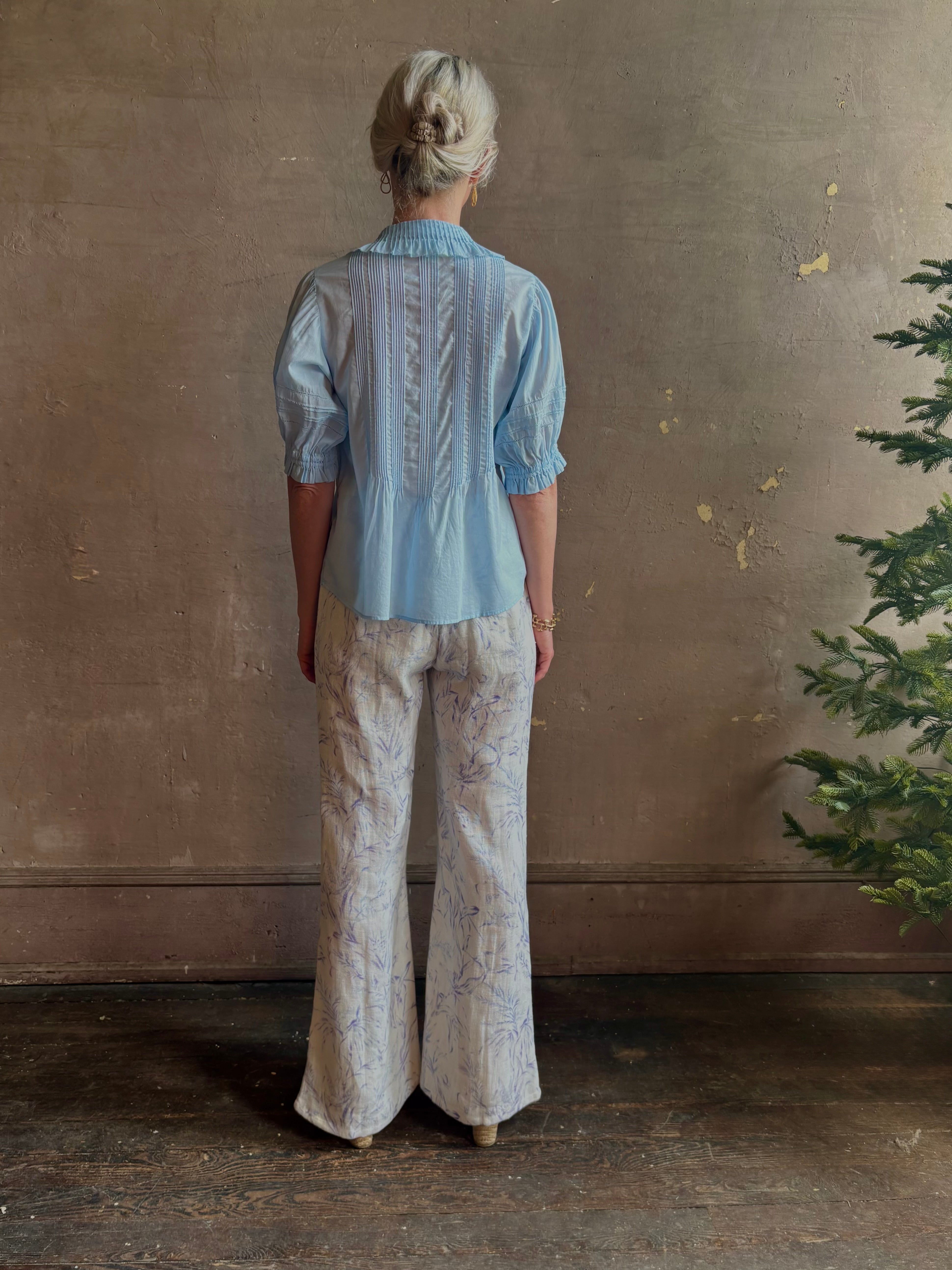 Mature woman wearing Jess Blouse from Trovata rendered in the light blur and crafted from cotton poplin with peter pan collar, half sleeves, intricate pitucking and button front