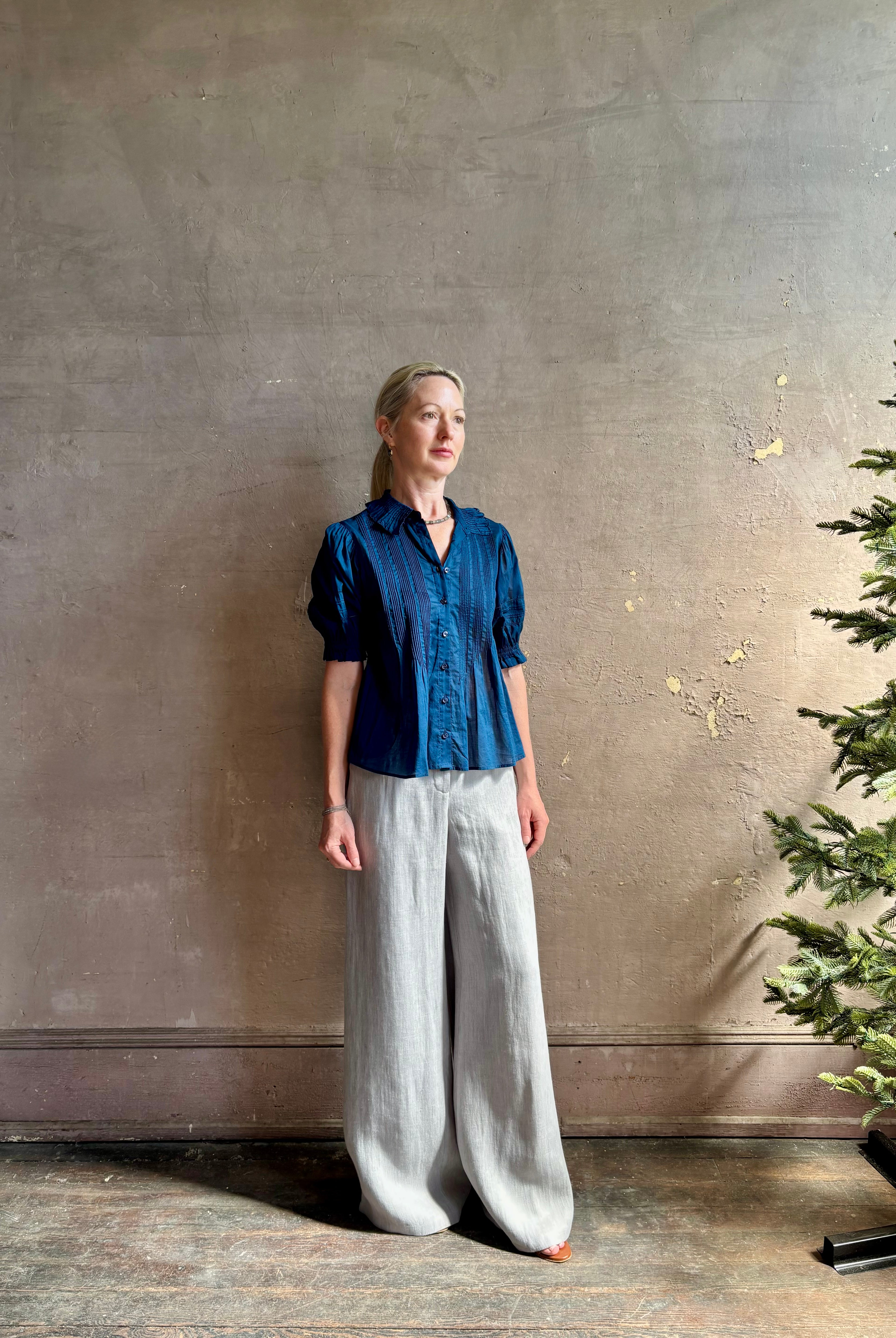 Mature woman wearing Jess Blouse from Trovata rendered in a classic Navy blue and crafted from light weight cotton poplin with short sleeves, peter pan collar, v-neck button front with intricate pintucking details at front and back