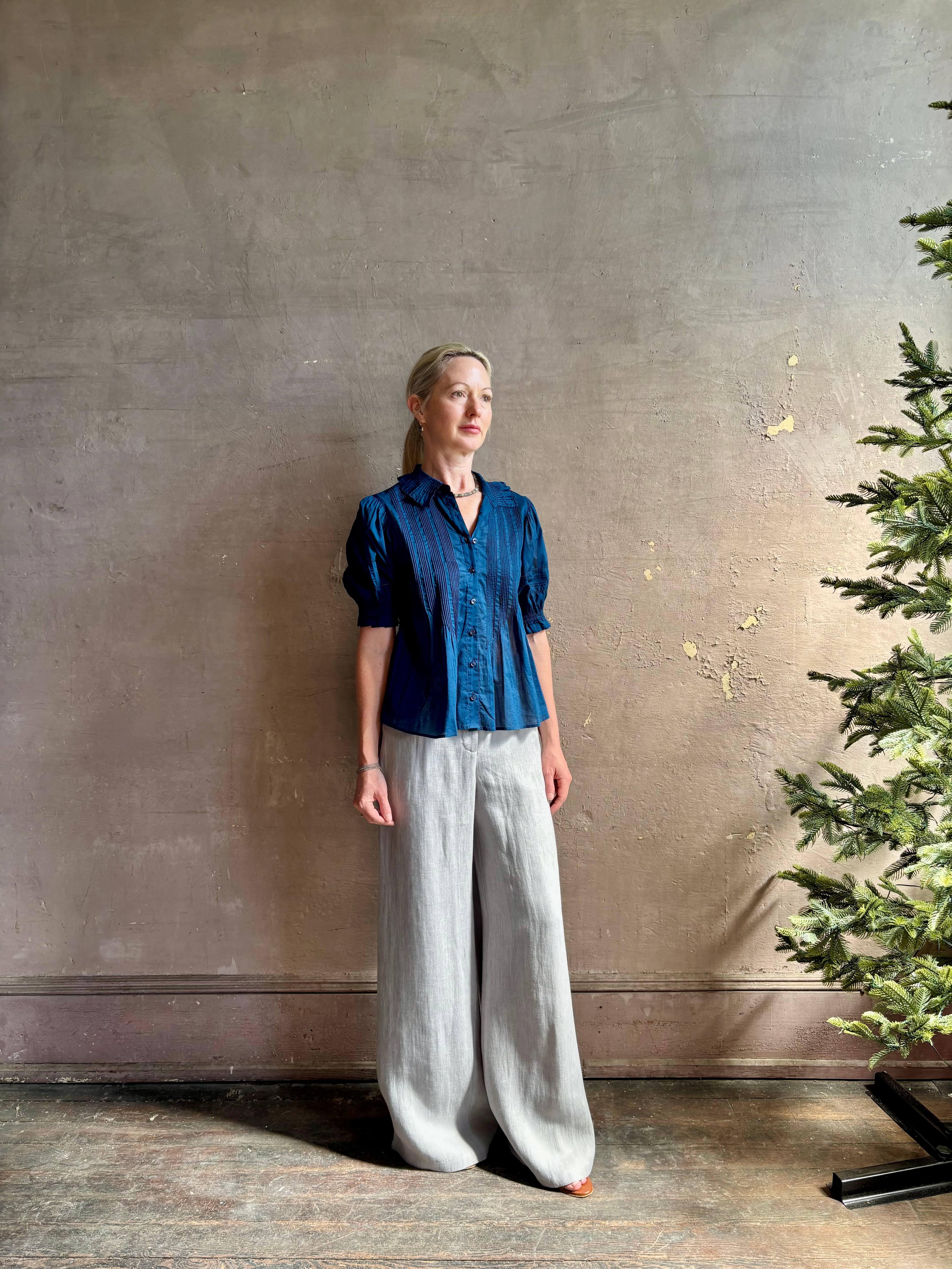 Mature woman wearing Jess Blouse from Trovata rendered in a classic Navy blue and crafted from light weight cotton poplin with short sleeves, peter pan collar, v-neck button front with intricate pintucking details at front and back