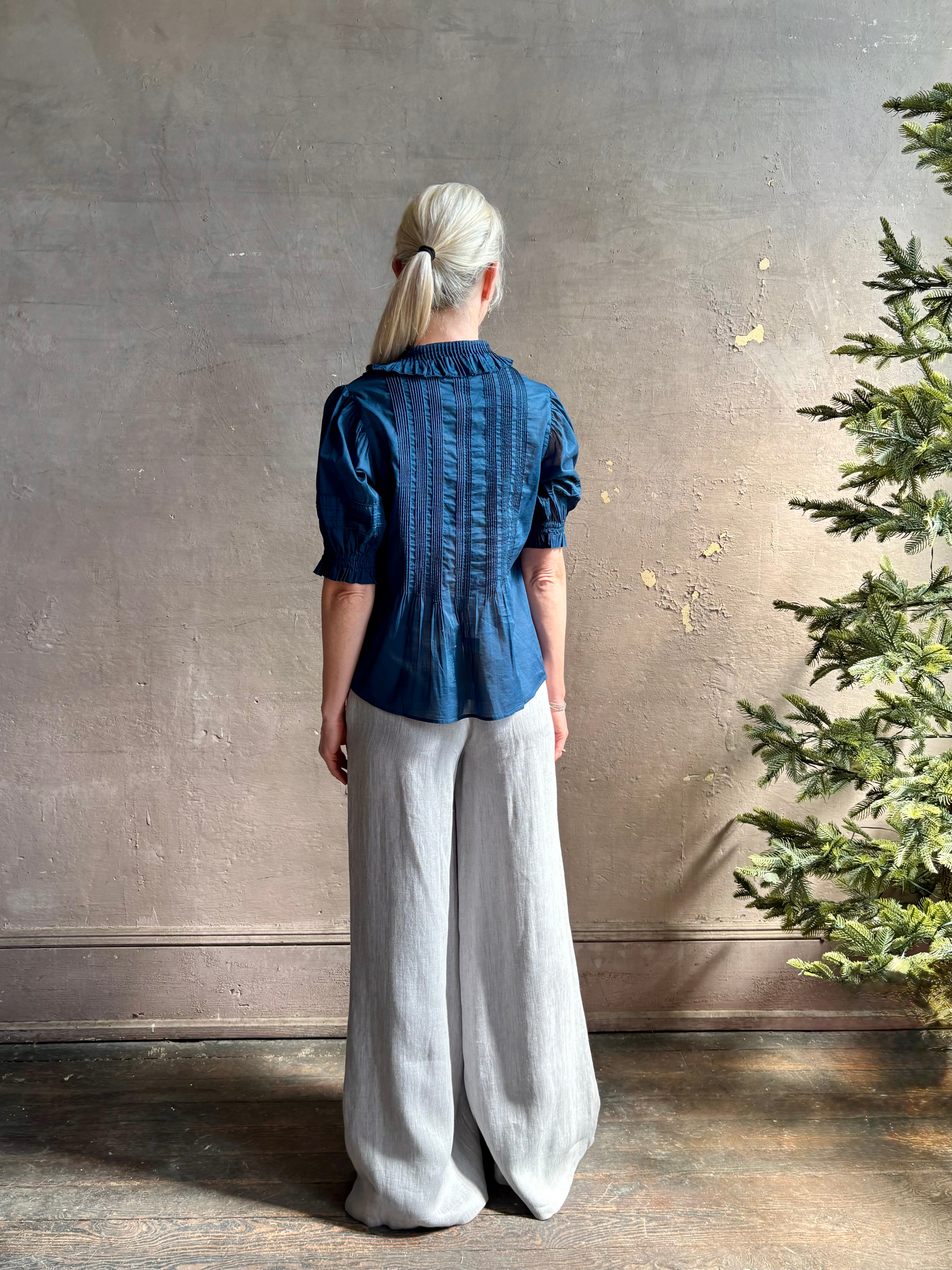 Mature woman wearing Jess Blouse from Trovata rendered in a classic Navy blue and crafted from light weight cotton poplin with short sleeves, peter pan collar, v-neck button front with intricate pintucking details at front and back