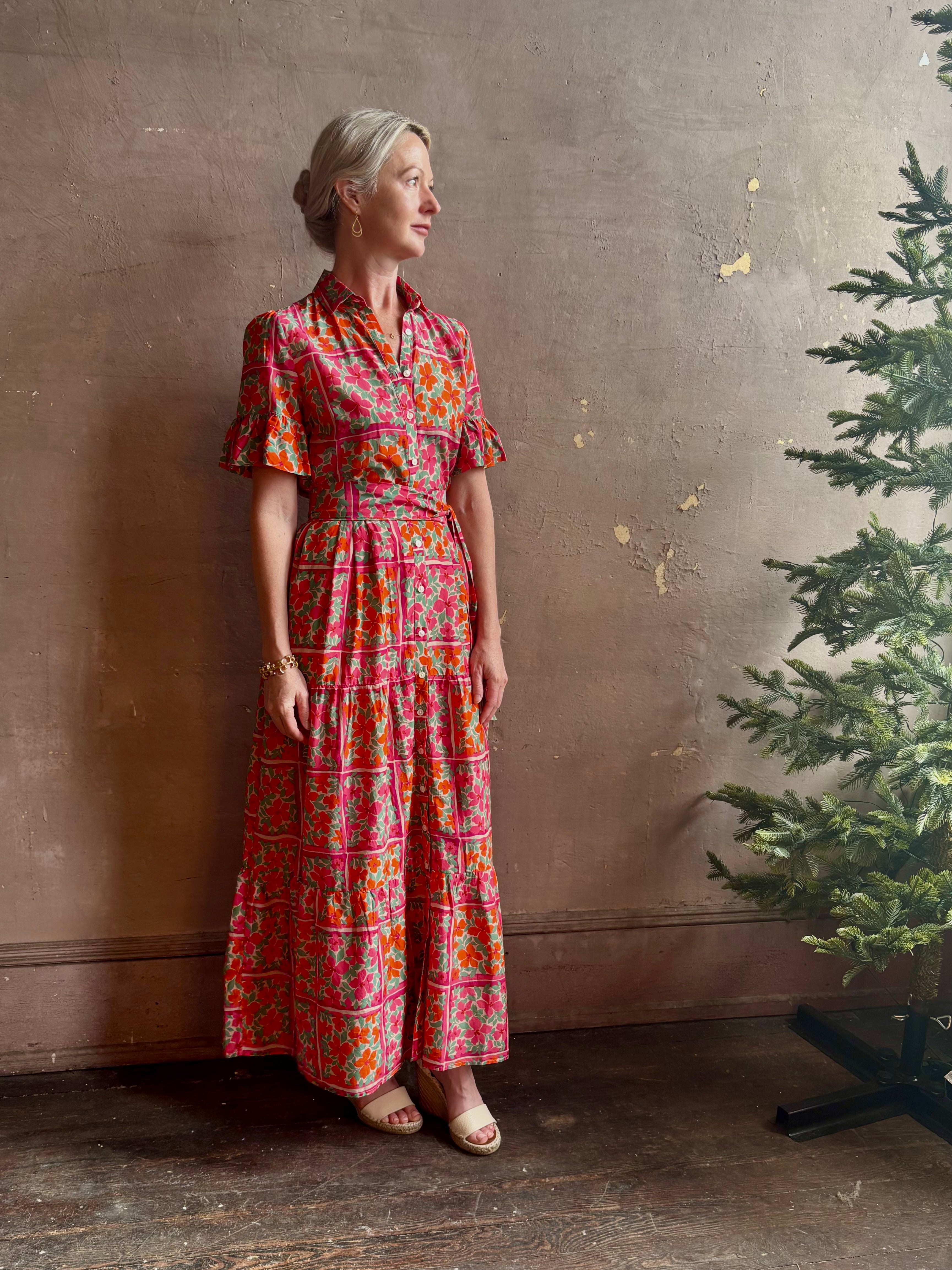 Mature woman wearing Martine maxi Dress from Trovata rendered in the Botanic Tile pink and orange floral print and crafted from a luxurious blend of cotton and silk with button front, collar, short sleeves and matching optional self tile belt