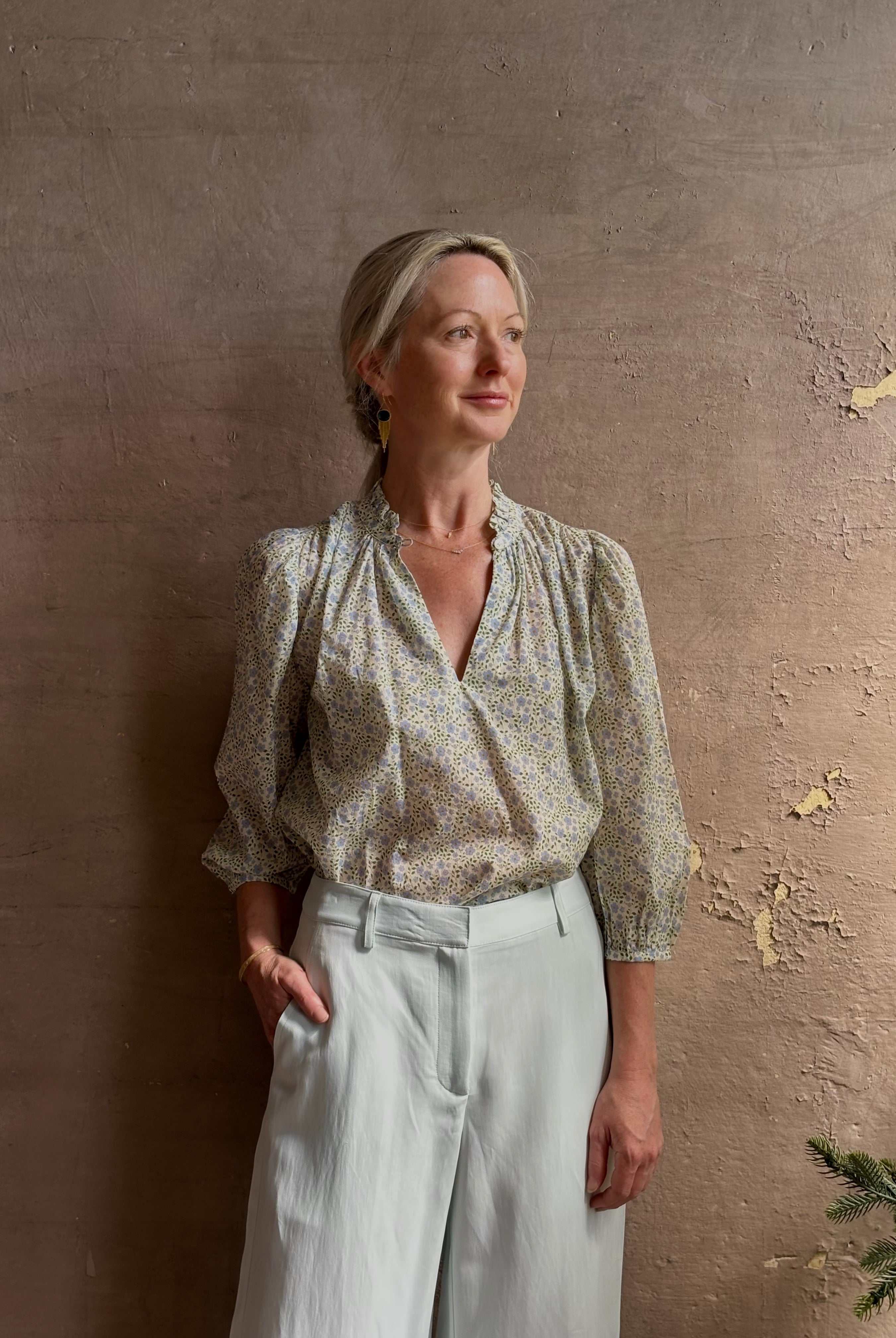 Mature woman wearing the Orly blouse from Trovata rendered in a charming coastal inspired floral print and crafted from cotton with three quarter sleeves and ruffle lined v-neck