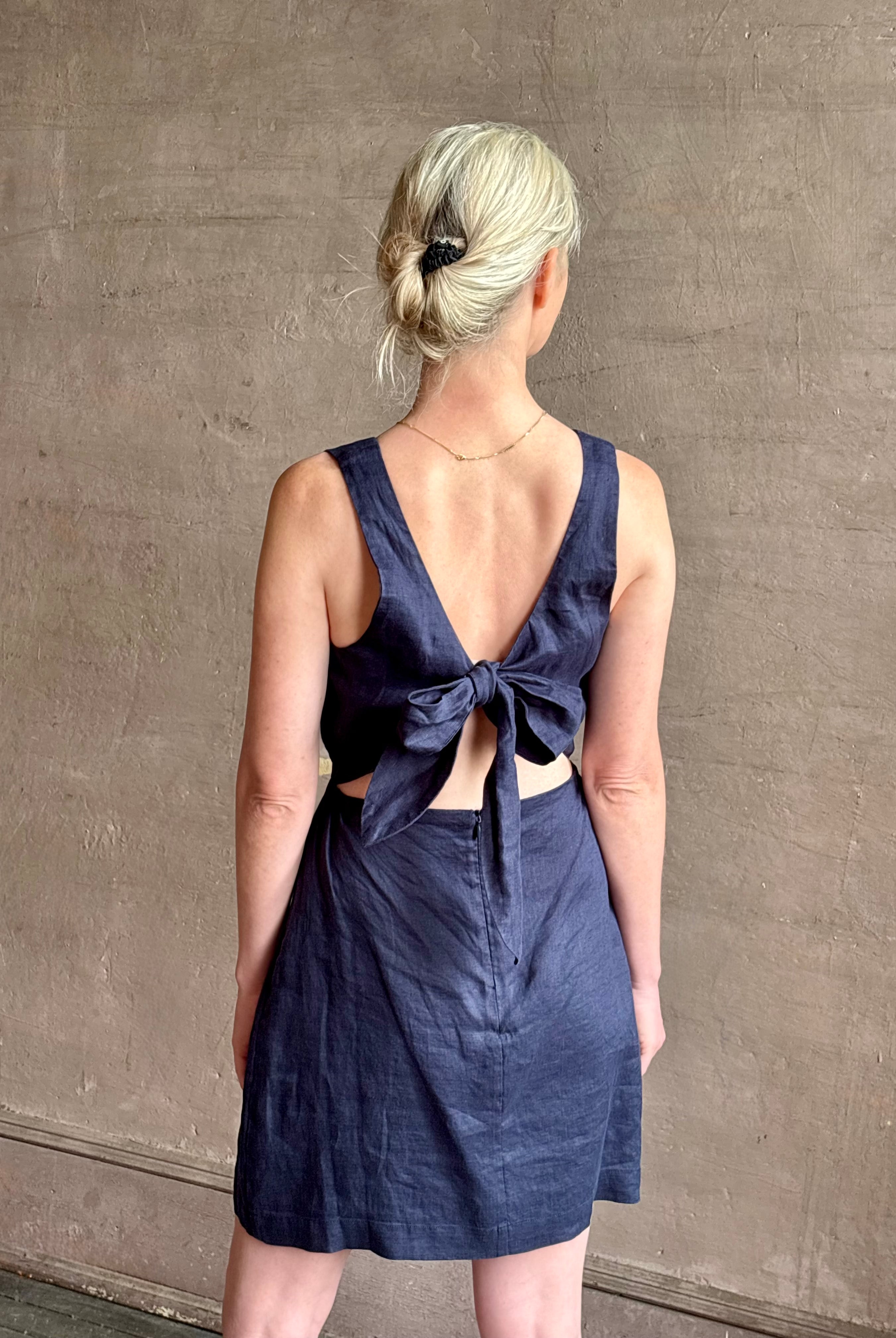 Woman wearing the effortless summer dress by Trovata Rosalie linen Dress in Navy Blue with A-line skirt and sophisticated bra friendly open back