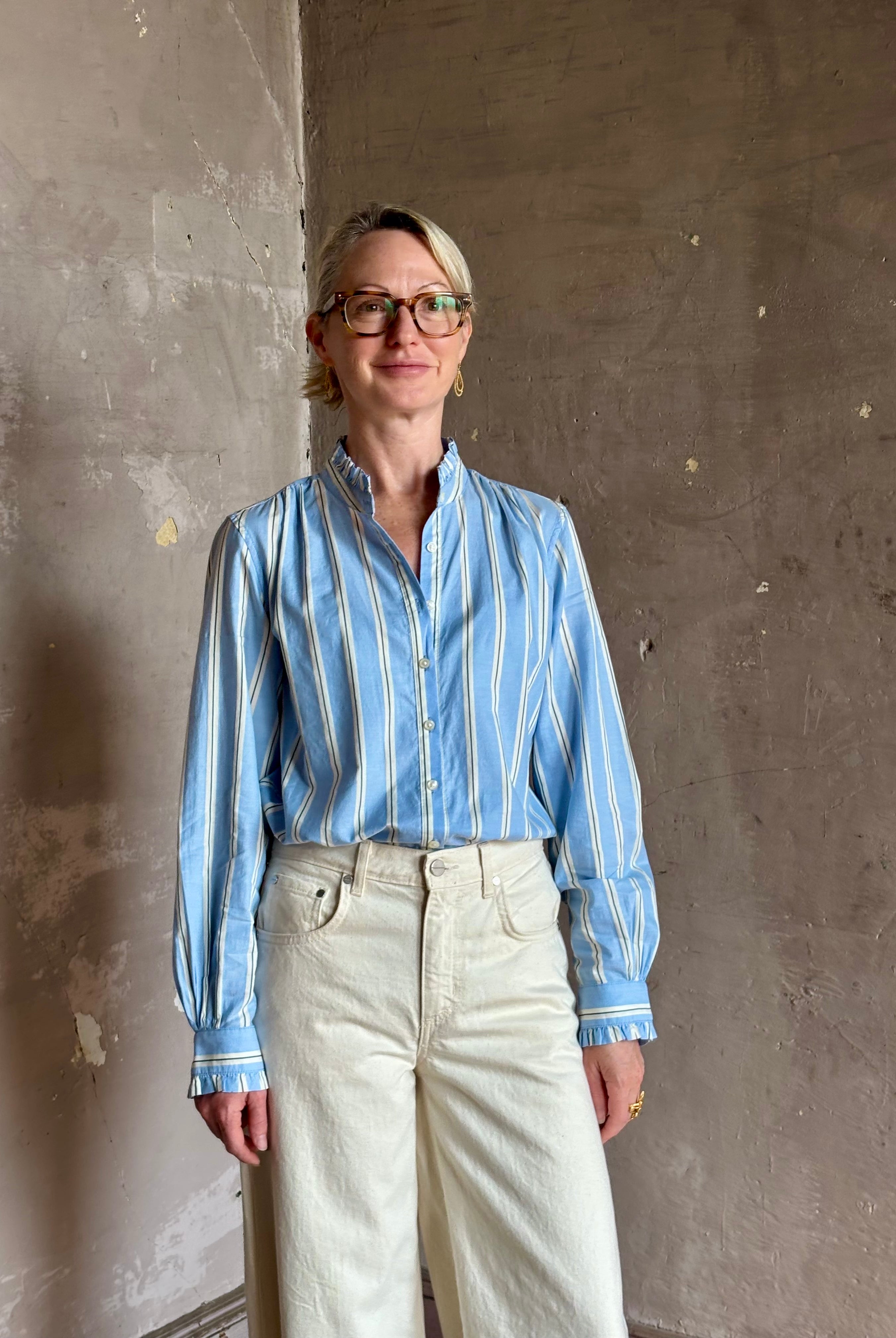 Mature woman in Trovata Rumi blue and cream vertically striped long-sleeve cotton shirt ruffle lined mandarin collar
