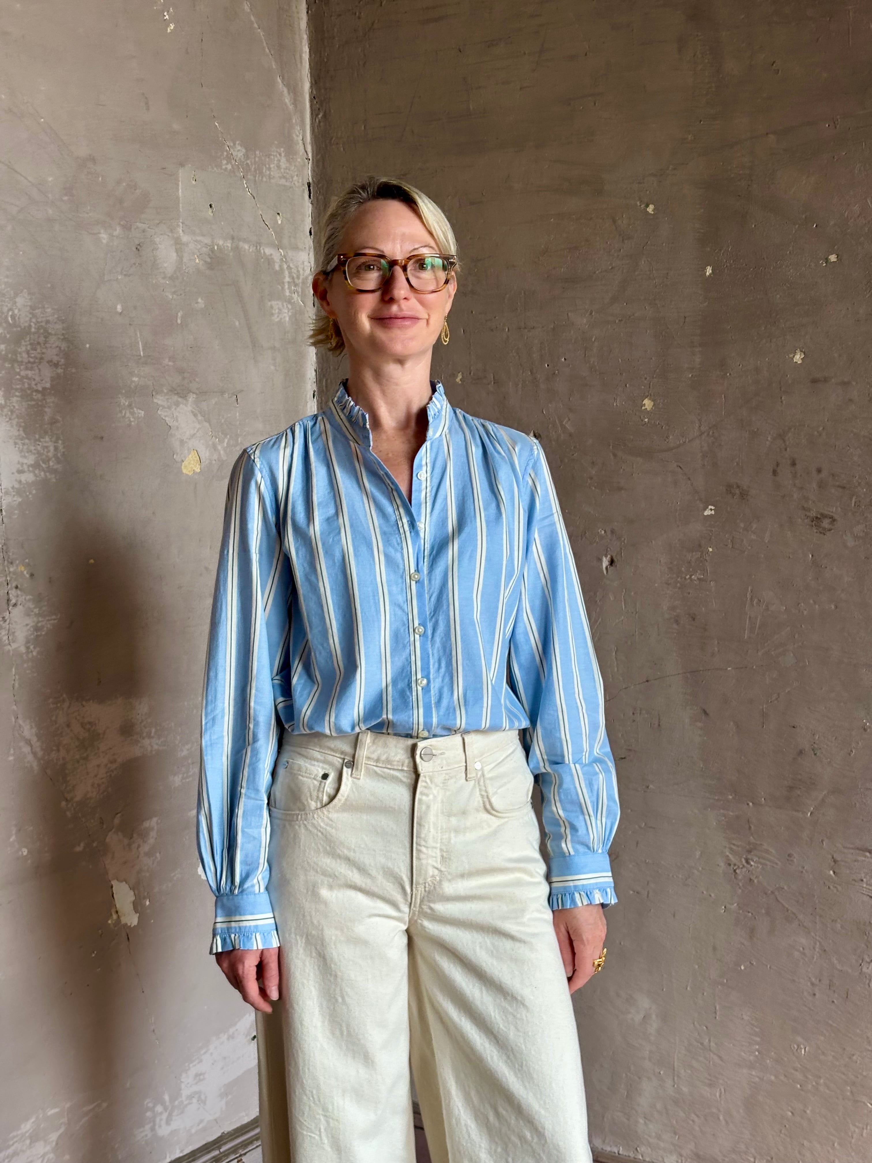 Mature woman in Trovata Rumi blue and cream vertically striped long-sleeve cotton shirt ruffle lined mandarin collar