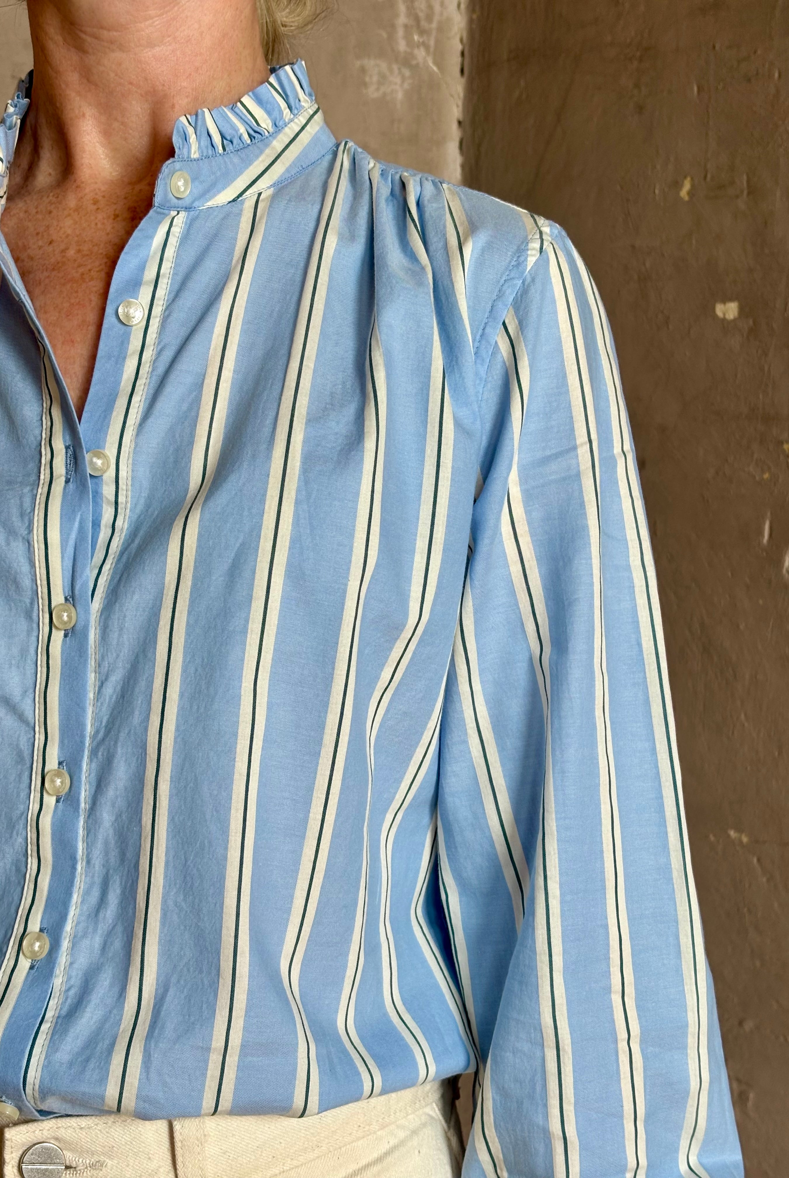 Mature woman wearing blue and cream vertically striped long-sleeve cotton Trovata Rumi shirt ruffle lined mandarin collar
