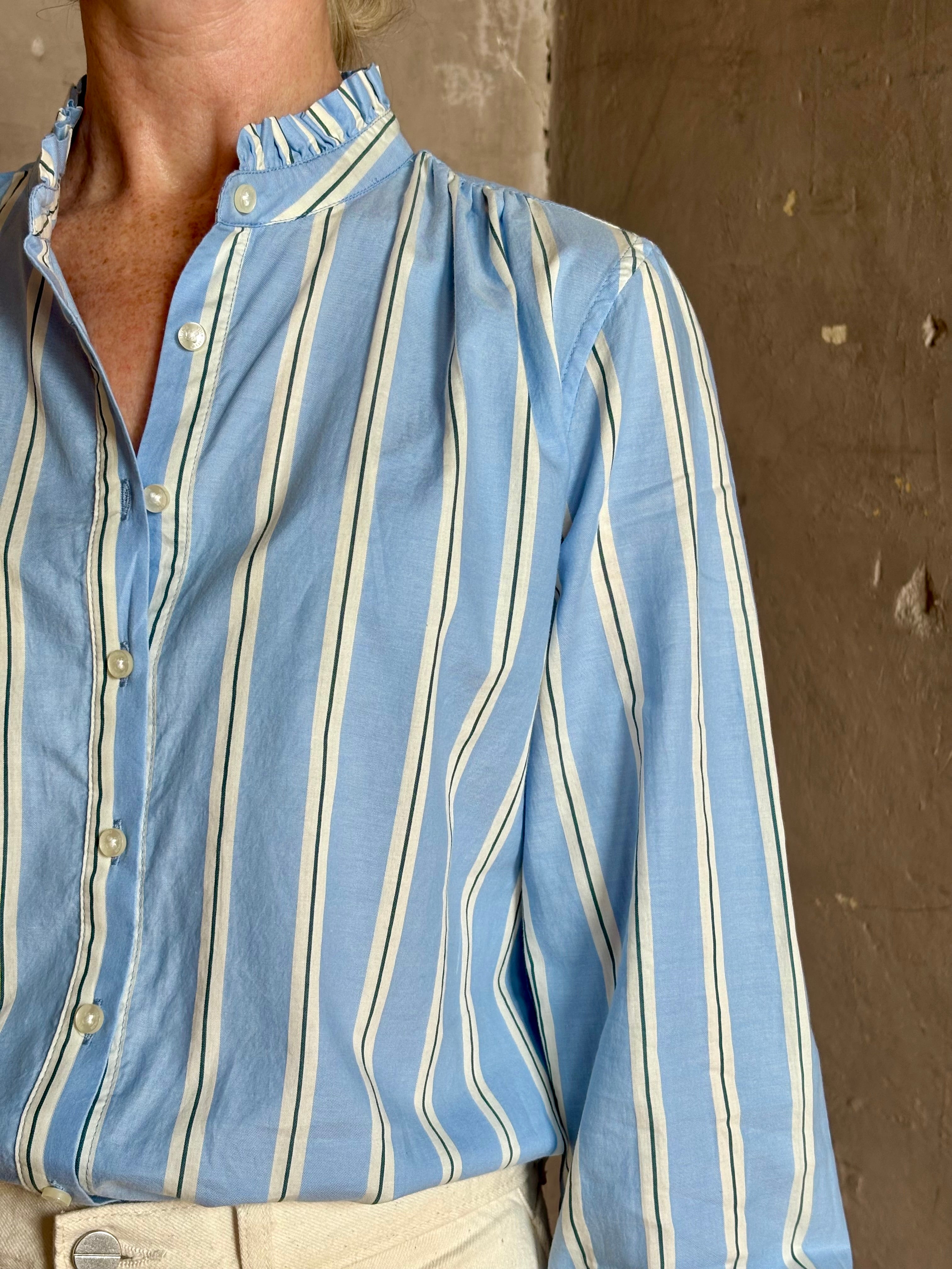 Mature woman wearing blue and cream vertically striped long-sleeve cotton Trovata Rumi shirt ruffle lined mandarin collar