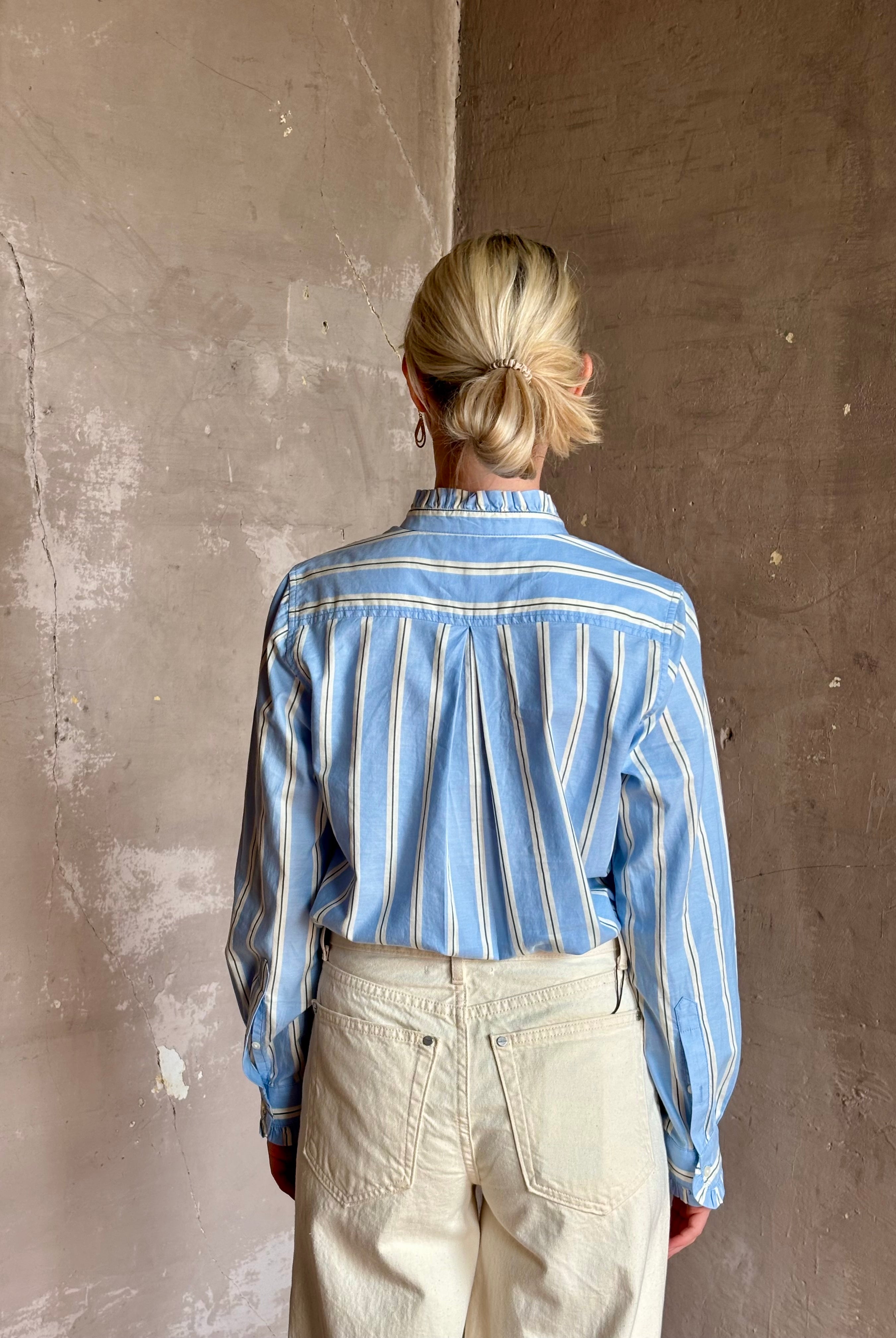 Mature woman wearing blue and cream vertically striped long-sleeve cotton Trovata Rumi shirt ruffle lined cuffs