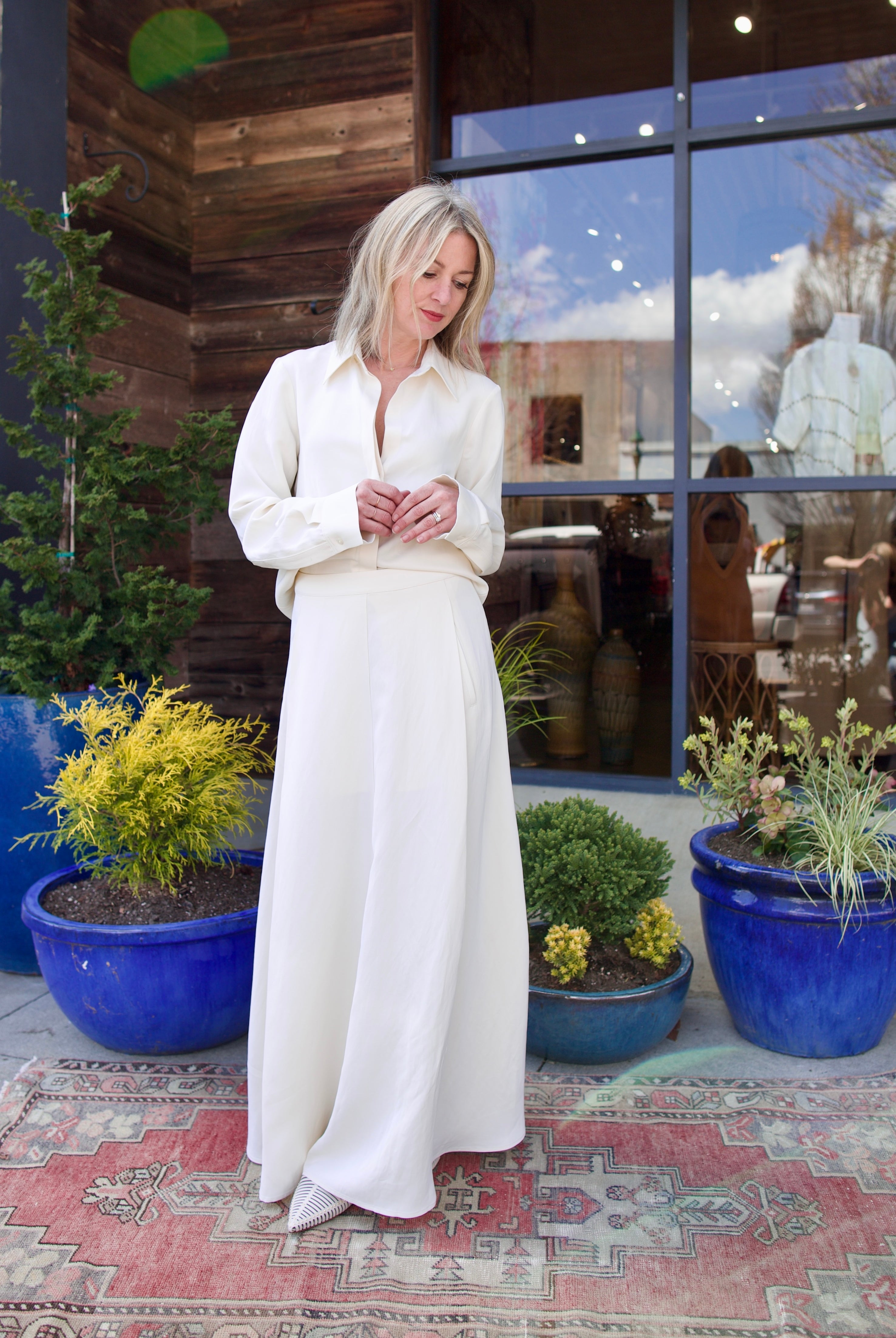 Image of mature woman wearing luxury brand TWP Cecelias coated linen pleated skirt with hidden seam pockets in elegant bone white