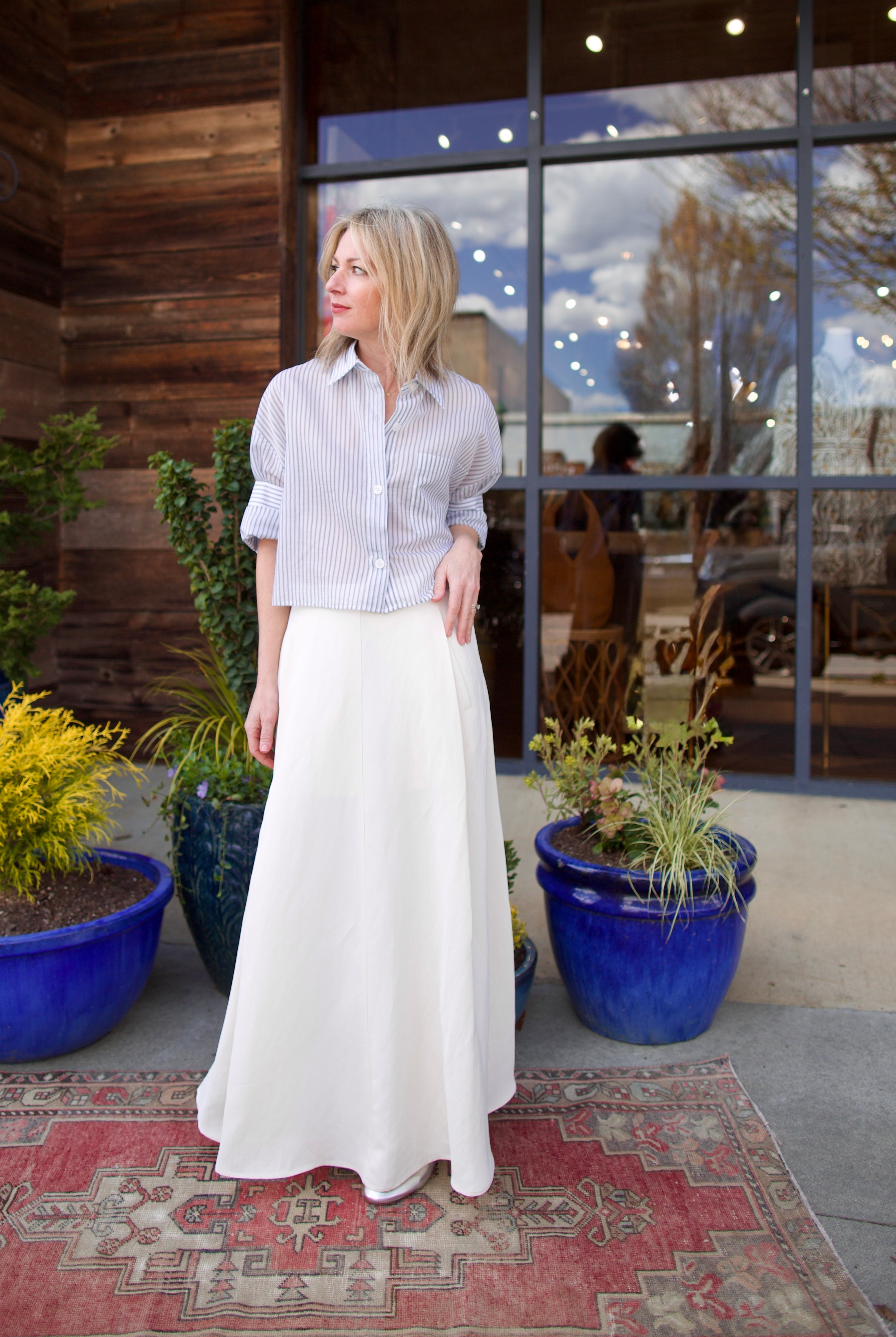 Image of mature woman wearing luxury brand TWP Cecelias coated linen pleated skirt with hidden seam pockets in elegant bone white