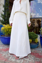 Image of mature woman wearing luxury brand TWP Cecelias coated linen pleated skirt with hidden seam pockets in elegant bone white
