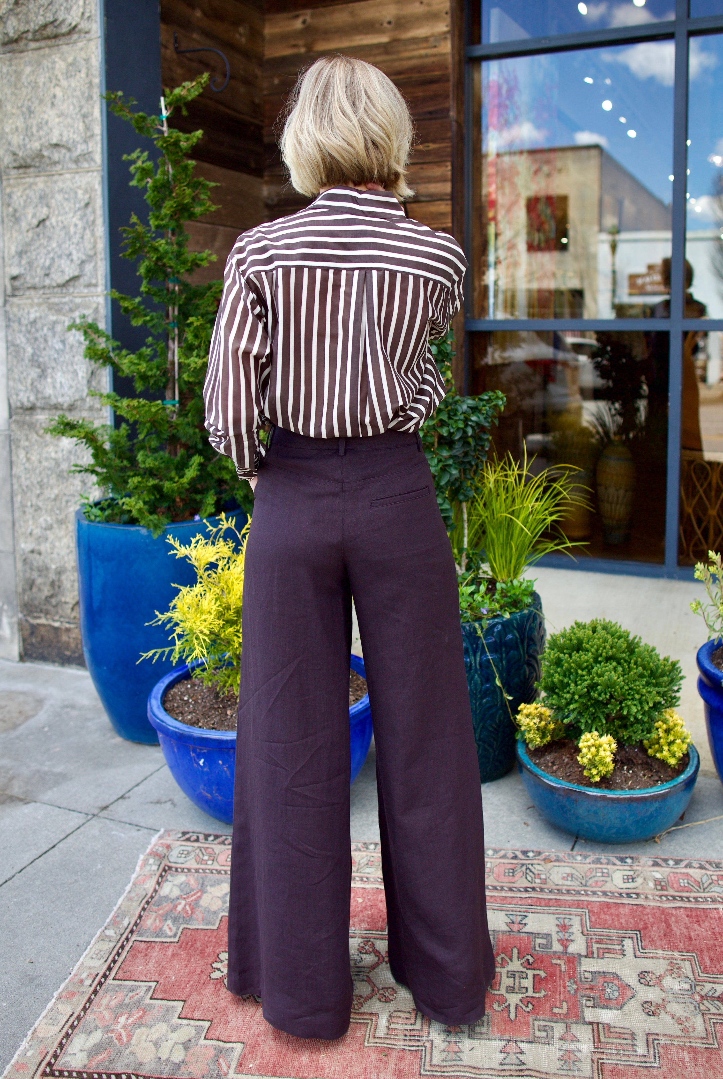 Image of model wearing luxury brand TWP Joey Striped blouse and Dees chocolate linen Trousers expertly tailored timeless elegance