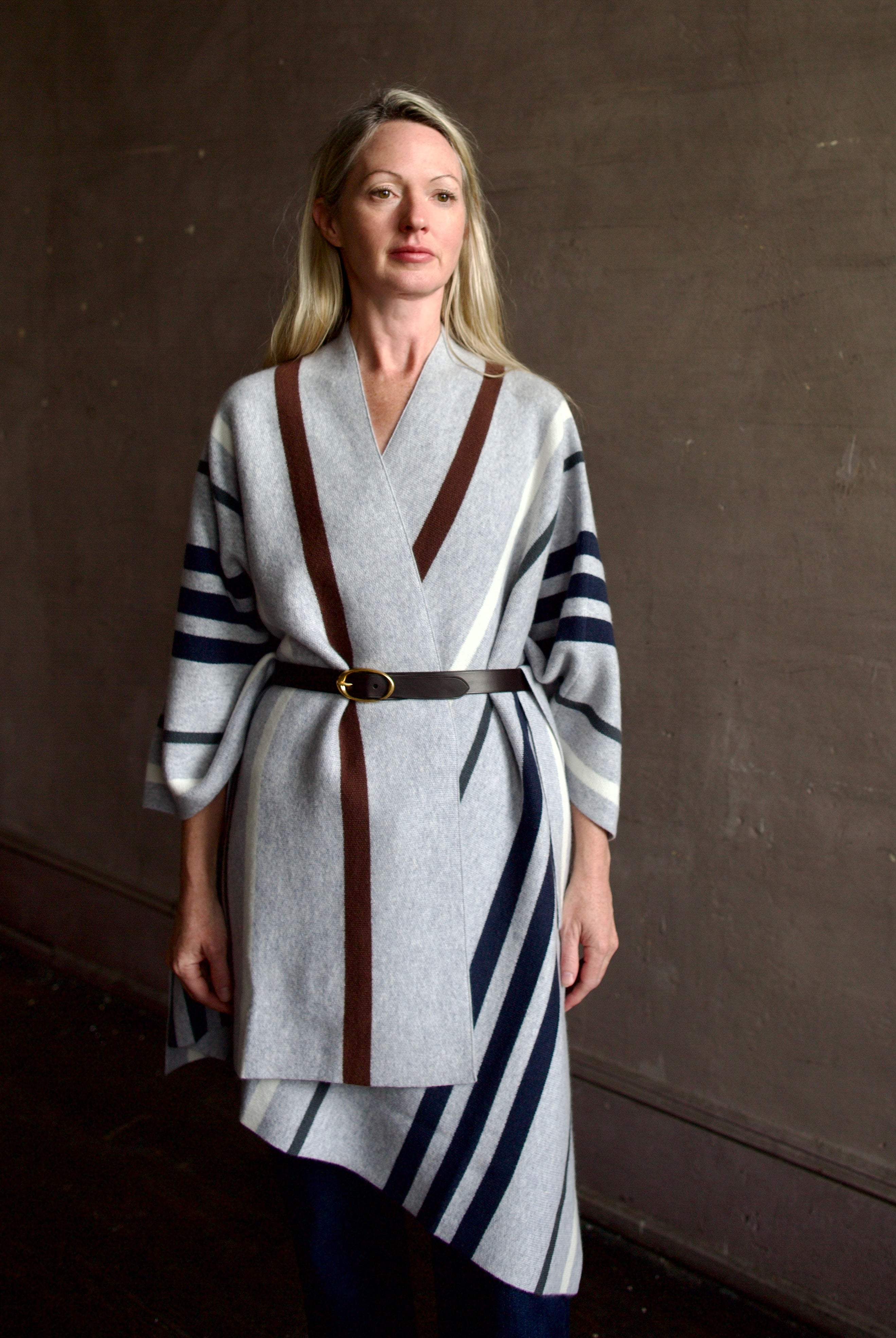 Mature Model wearing gray TWP luxury Italian cashmere poncho with brown and navy stripes and a leather belt