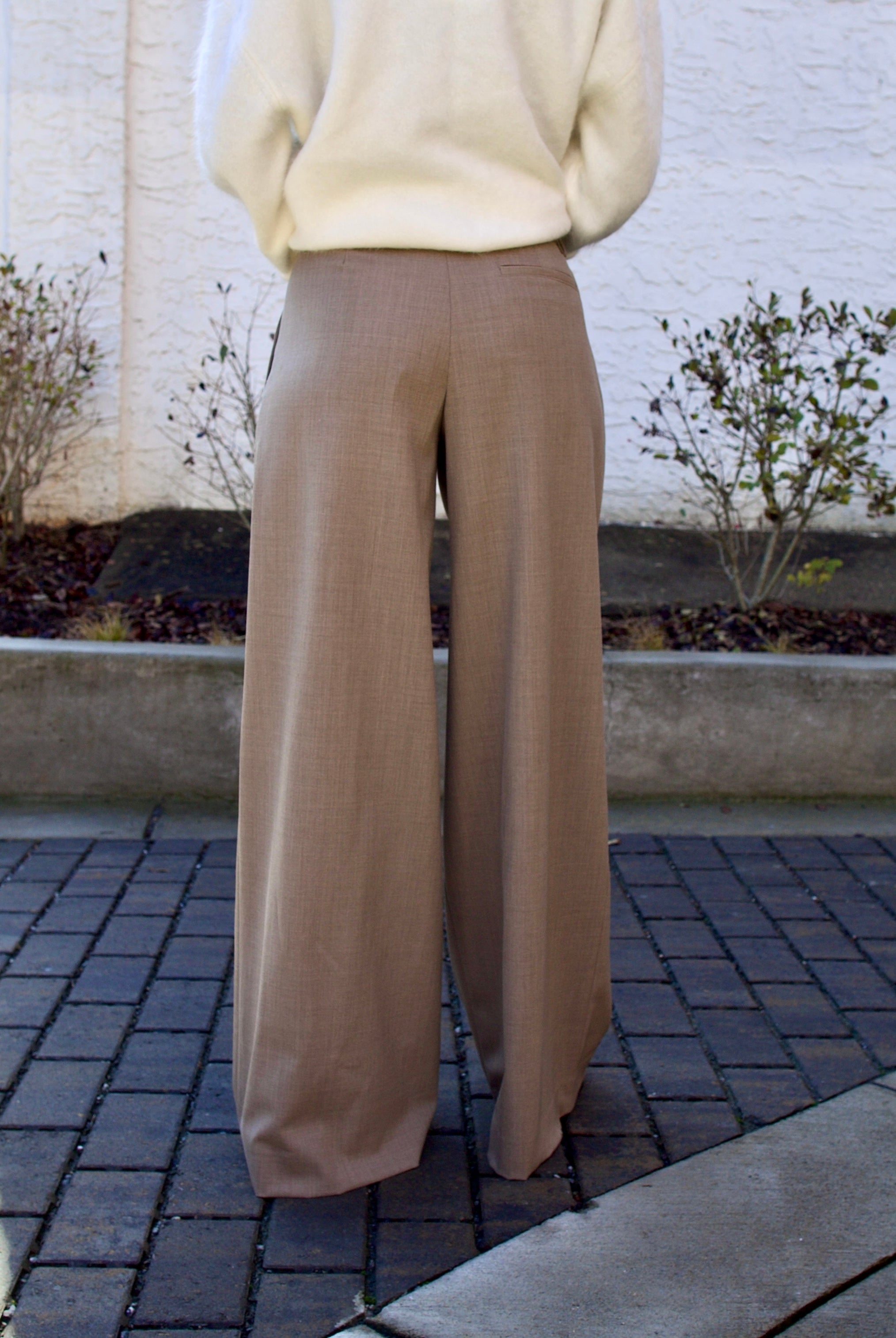 Image of the back of a woman wearing the TWP new didi pants in sandstone, the Ulla Johnson gia belt, and the Lisa Yang Margareta sweater.