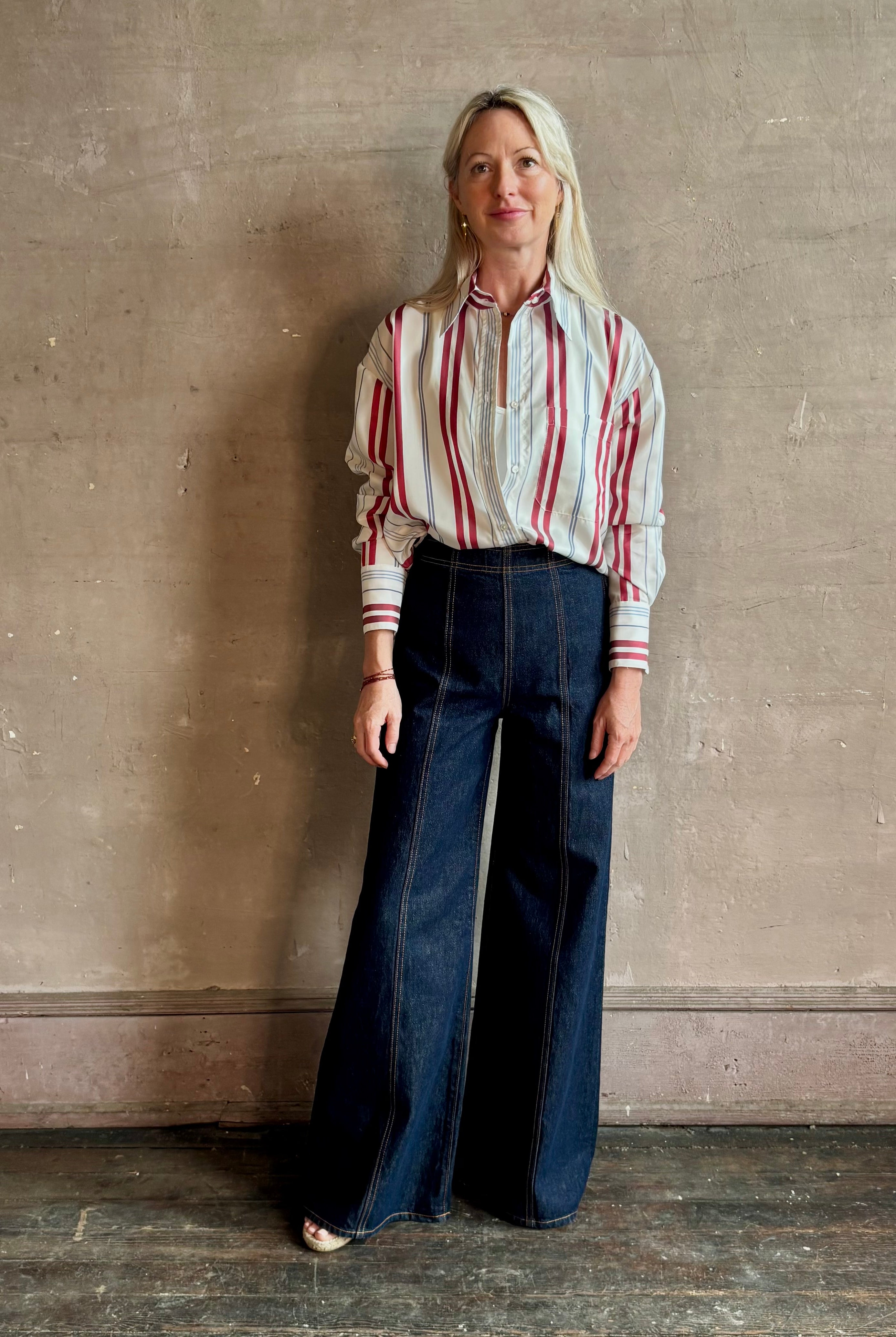 Mature woman wearing Big Joe Shirt from TWP rendered in an ivory, blue, and wine striped colorway and crafted from silk in the USA with collar, button front and wide cuffed long sleeves in a generous oversized fit