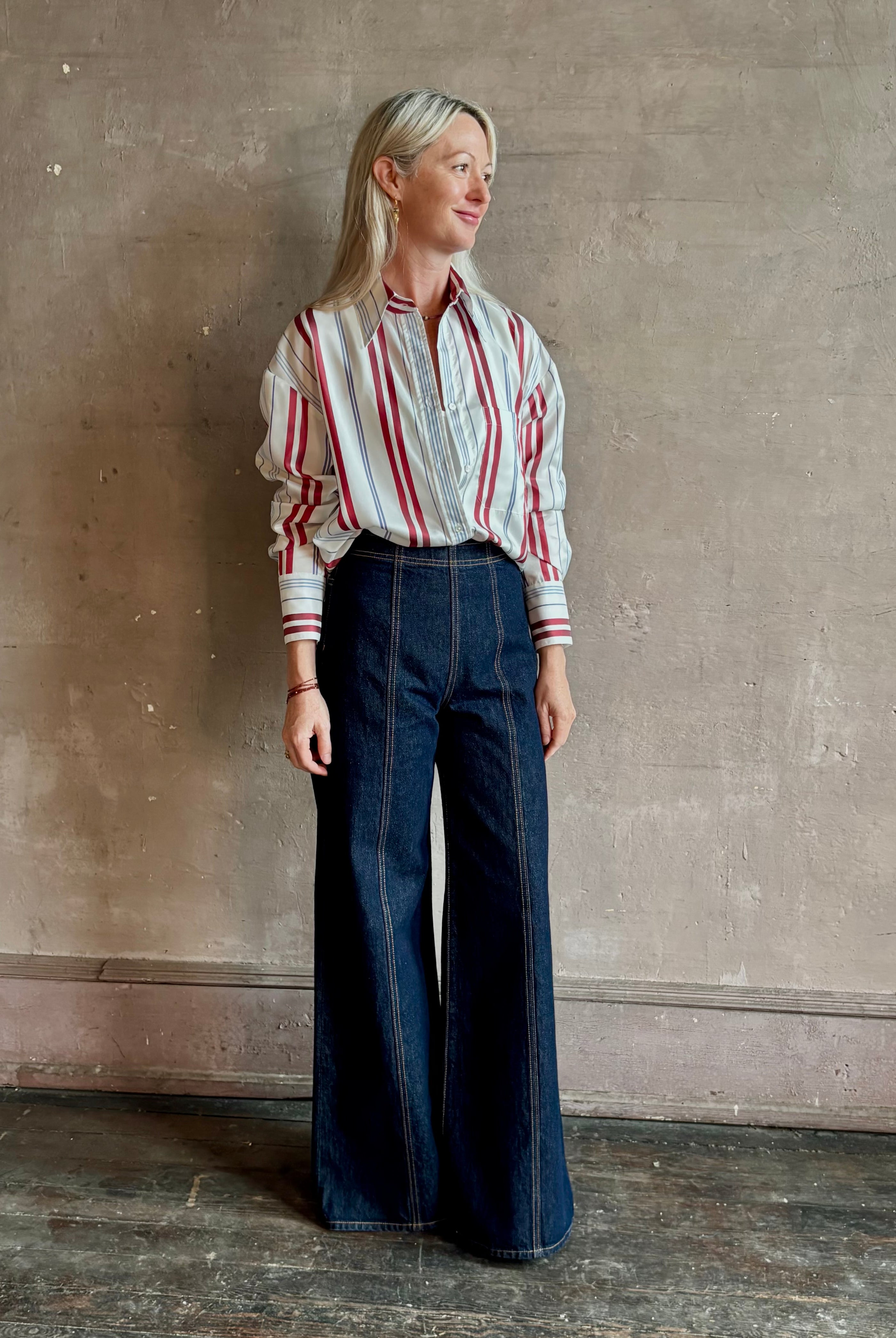 Mature woman wearing Big Joe Shirt from TWP rendered in an ivory, blue, and wine striped colorway and crafted from silk in the USA with collar, button front and wide cuffed long sleeves in a generous oversized fit