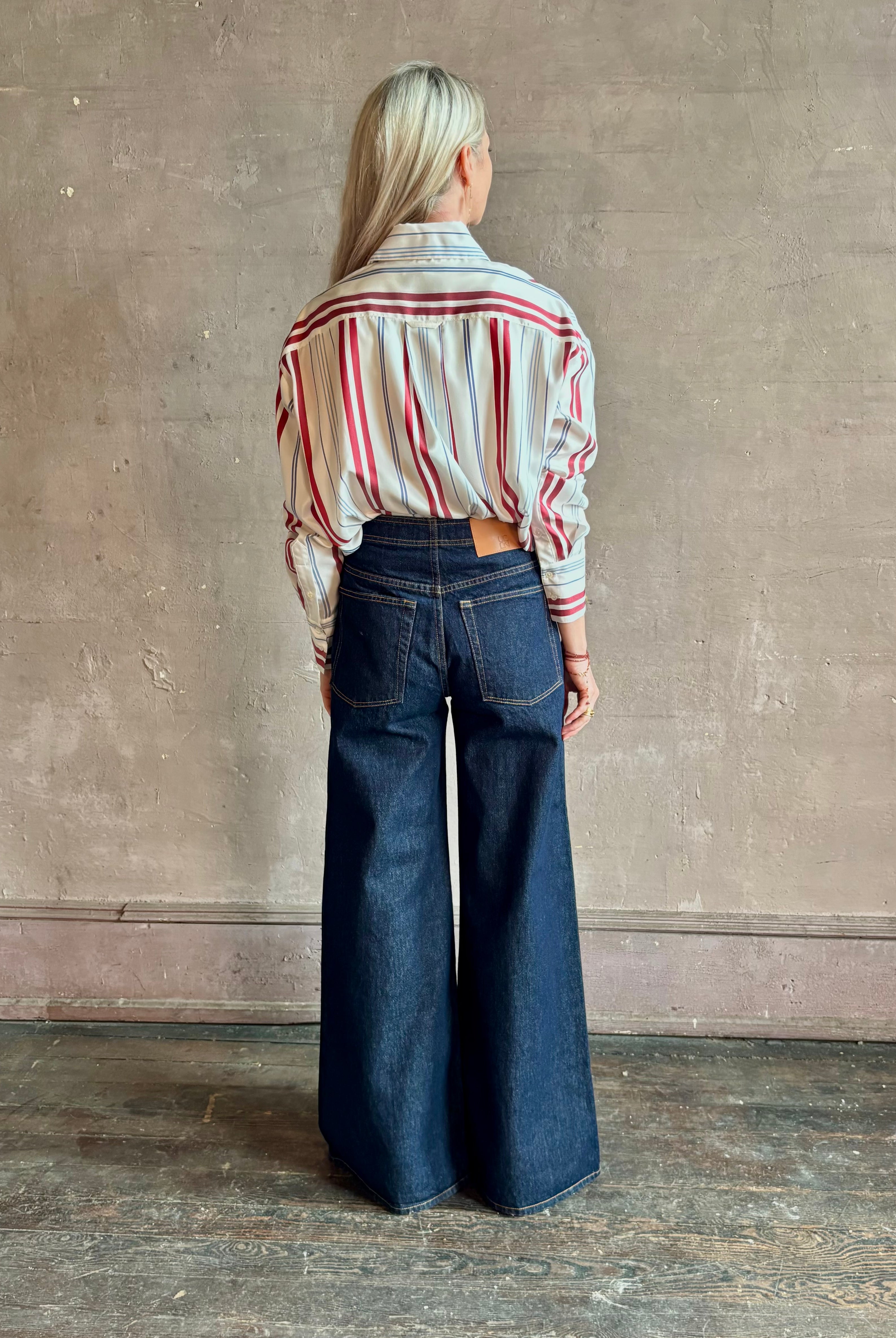 Mature woman wearing Big Joe Shirt from TWP rendered in an ivory, blue, and wine striped colorway and crafted from silk in the USA with collar, button front and wide cuffed long sleeves in a generous oversized fit