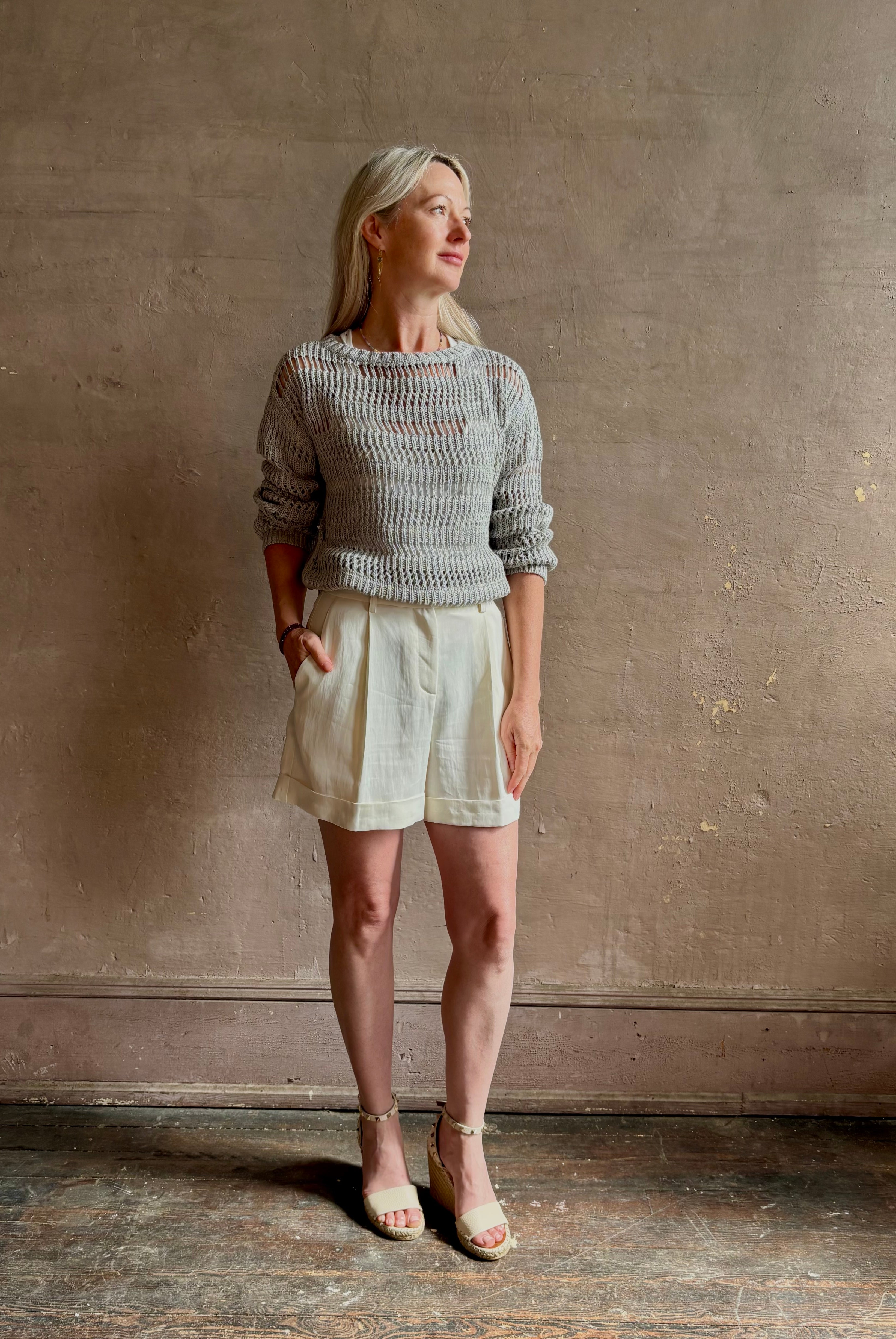 Mature woman wearing elevated tailored Cisco Shorts from TWP rendered in a soft bone white and crafted in the USA using a viscose and linen blend fabric with side seam pockets, belt loops, single front pleat and cuffed at the bottom