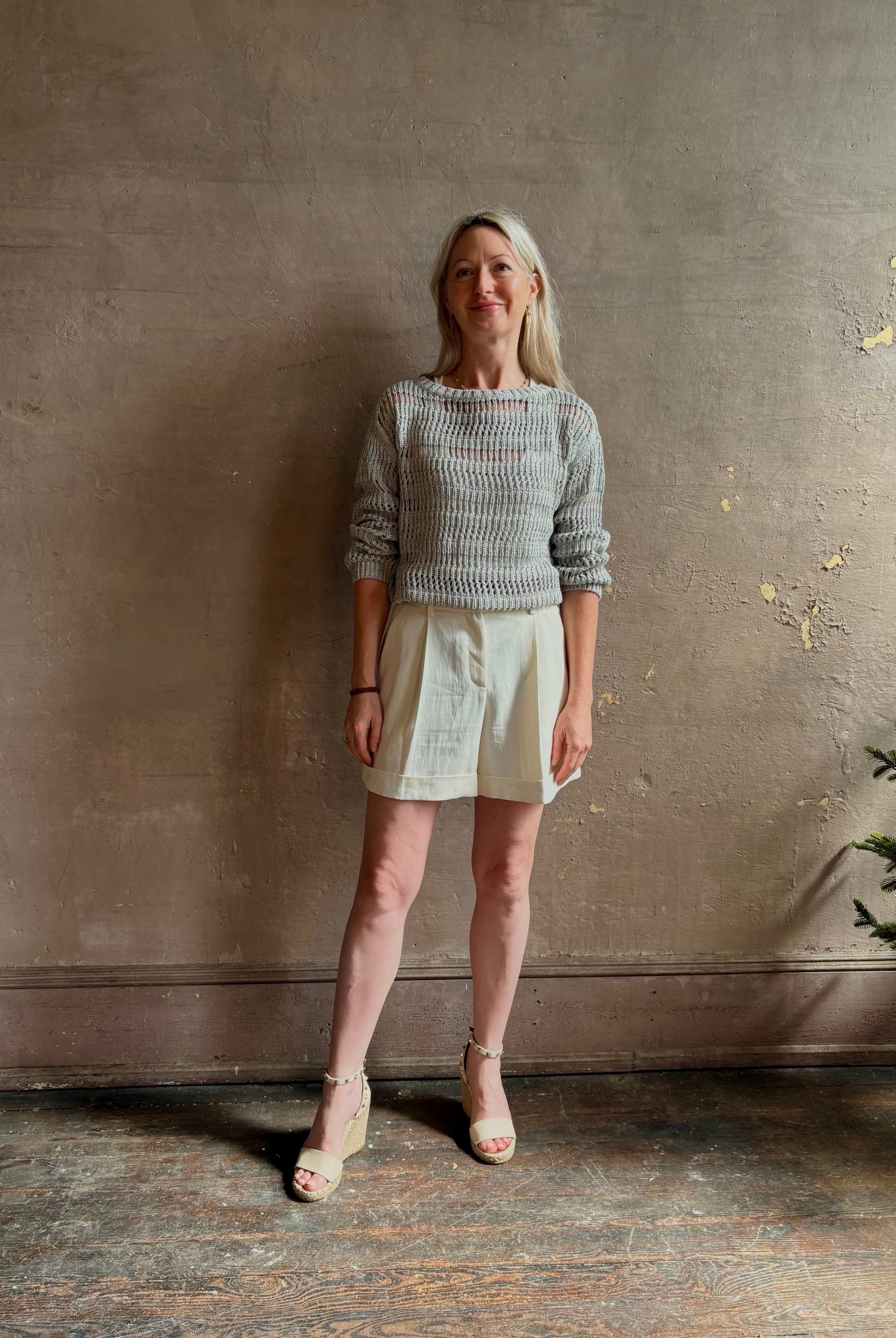 Mature woman wearing elevated tailored Cisco Shorts from TWP rendered in a soft bone white and crafted in the USA using a viscose and linen blend fabric with side seam pockets, belt loops, single front pleat and cuffed at the bottom