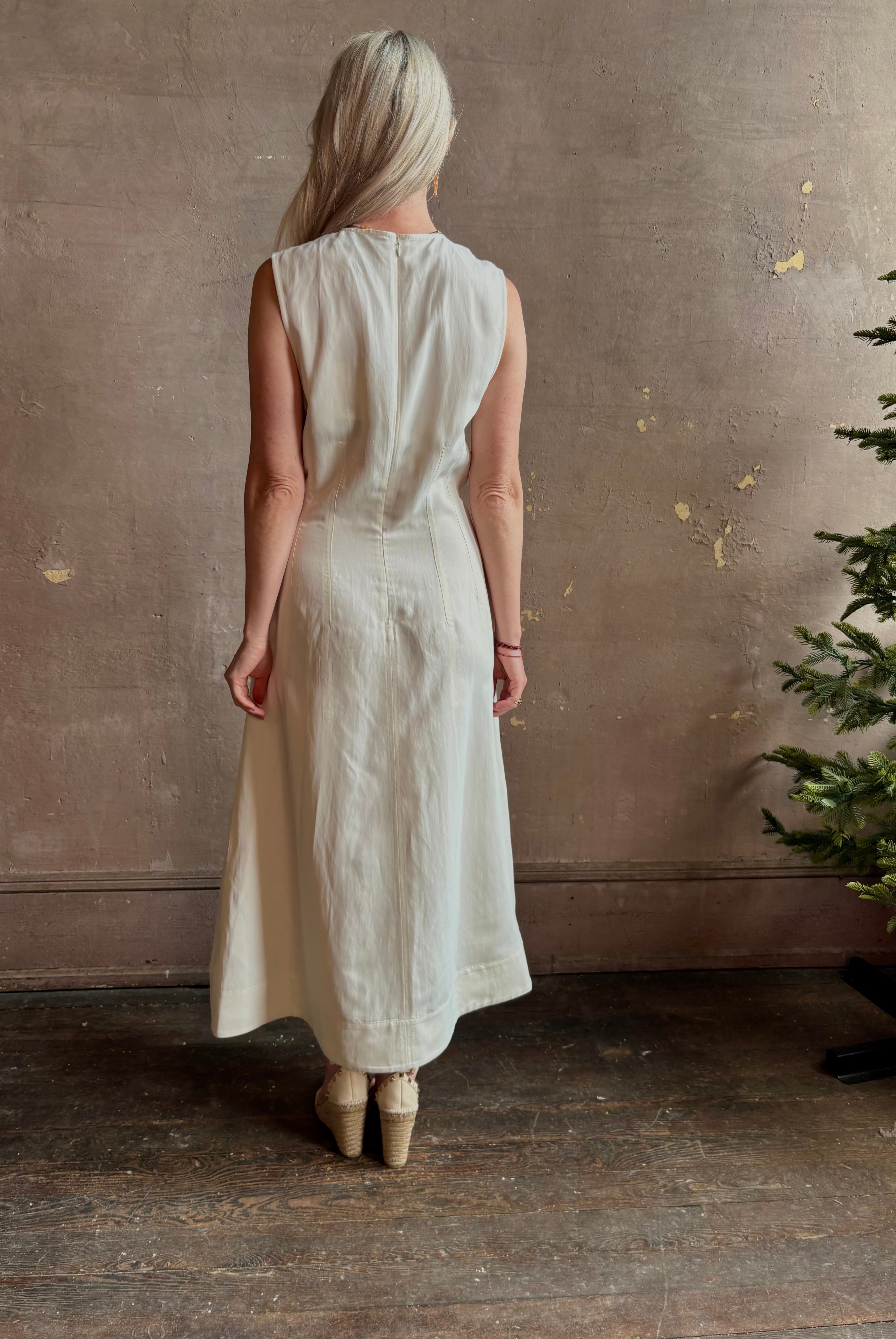 Mature woman wearing elegant Crew Neck maxi A-Line Dress with Darts from TWP rendered in a soft off white and crafted in the USA from a viscose and linen fabric blend with side seam pockets and sleeveless
