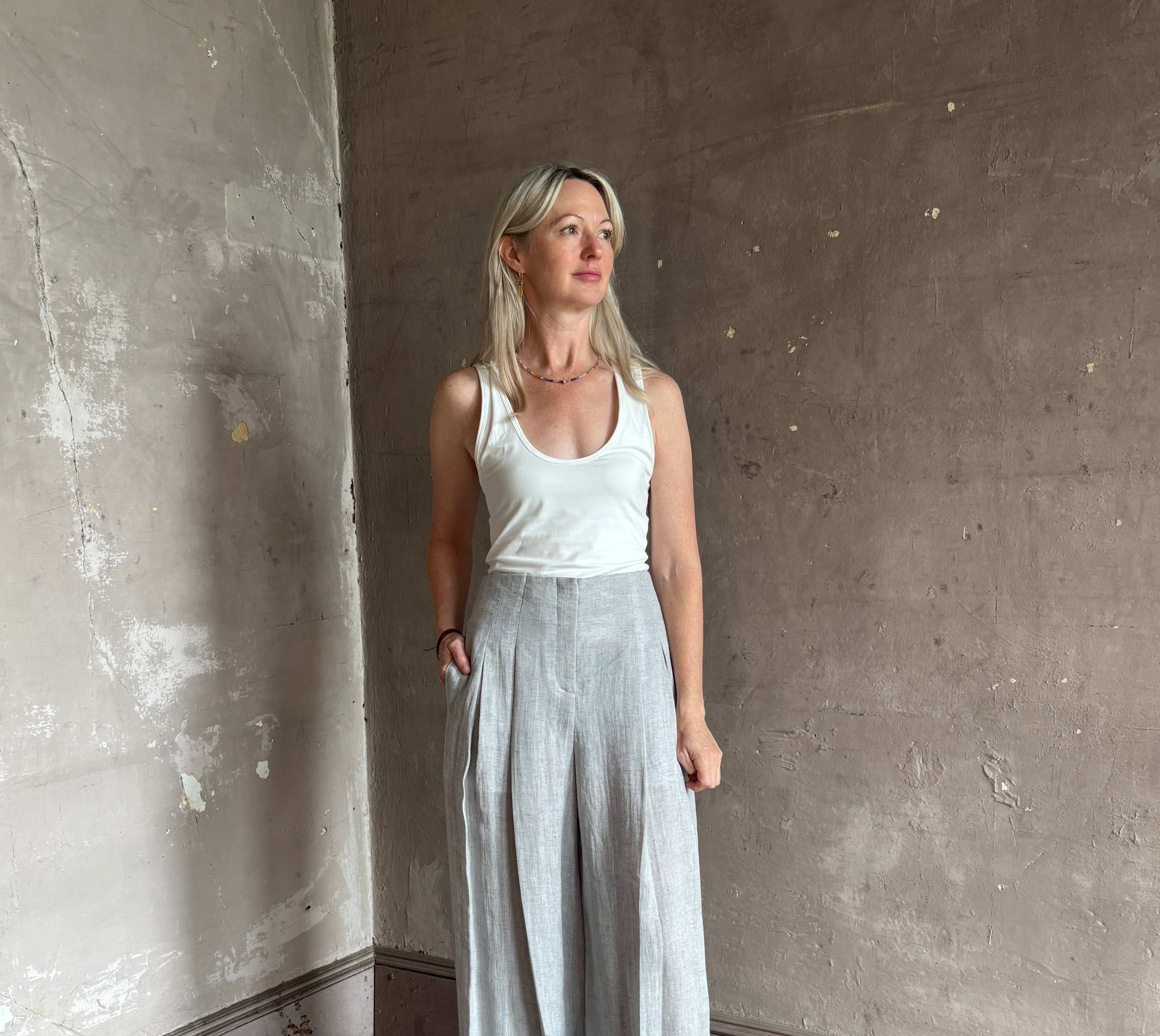 Mature woman wearing effortless women's designer Drew wide leg Trouser from TWP rendered in a versatile light heather grey and crafted from light weight hemp with high-rise, drop waist pleats, and side seam pockets, and made in the USA
